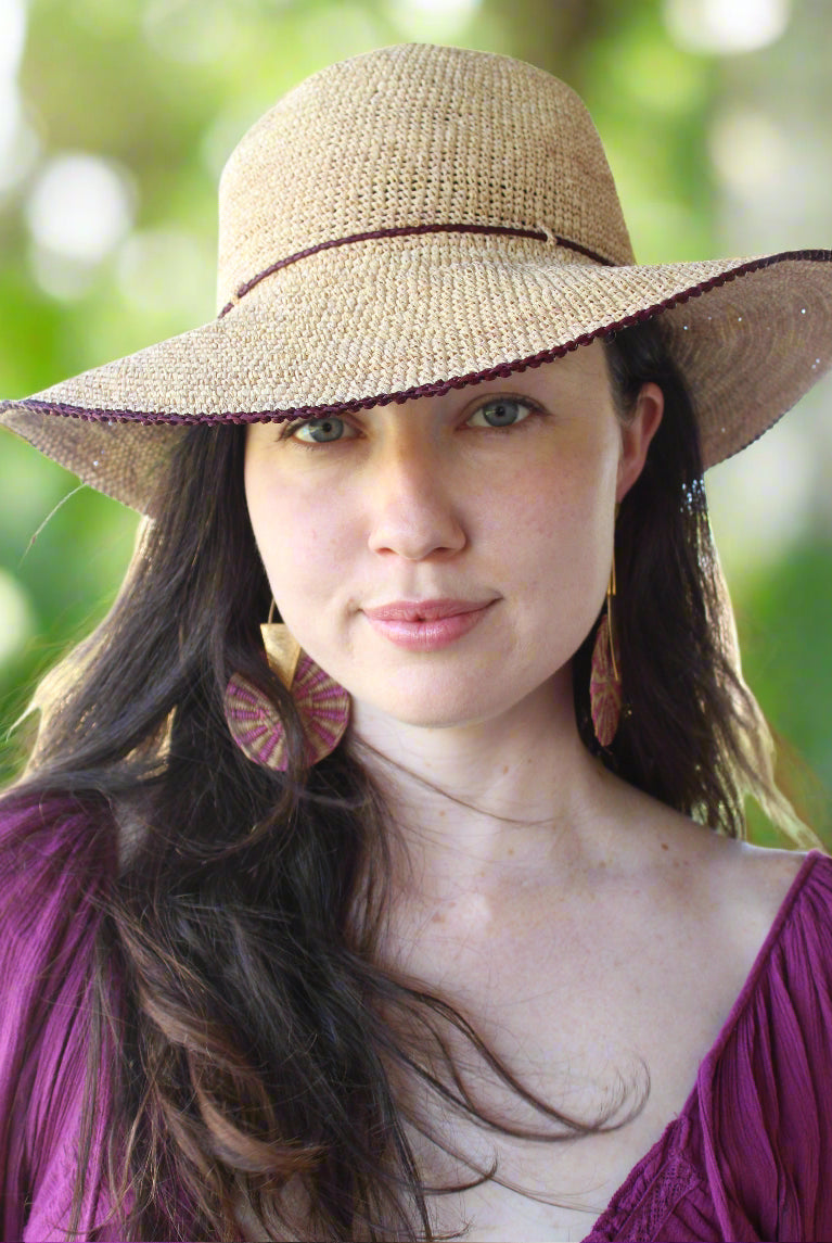 Model wearing 4 inch brim Rachel Crochet Umberwine handmade straw sun hat umberwine bordeaux/claret/deep/dark/red/purple trim woven edge and matching adjustable hat band on natural straw colored raffia hat - Shebobo
