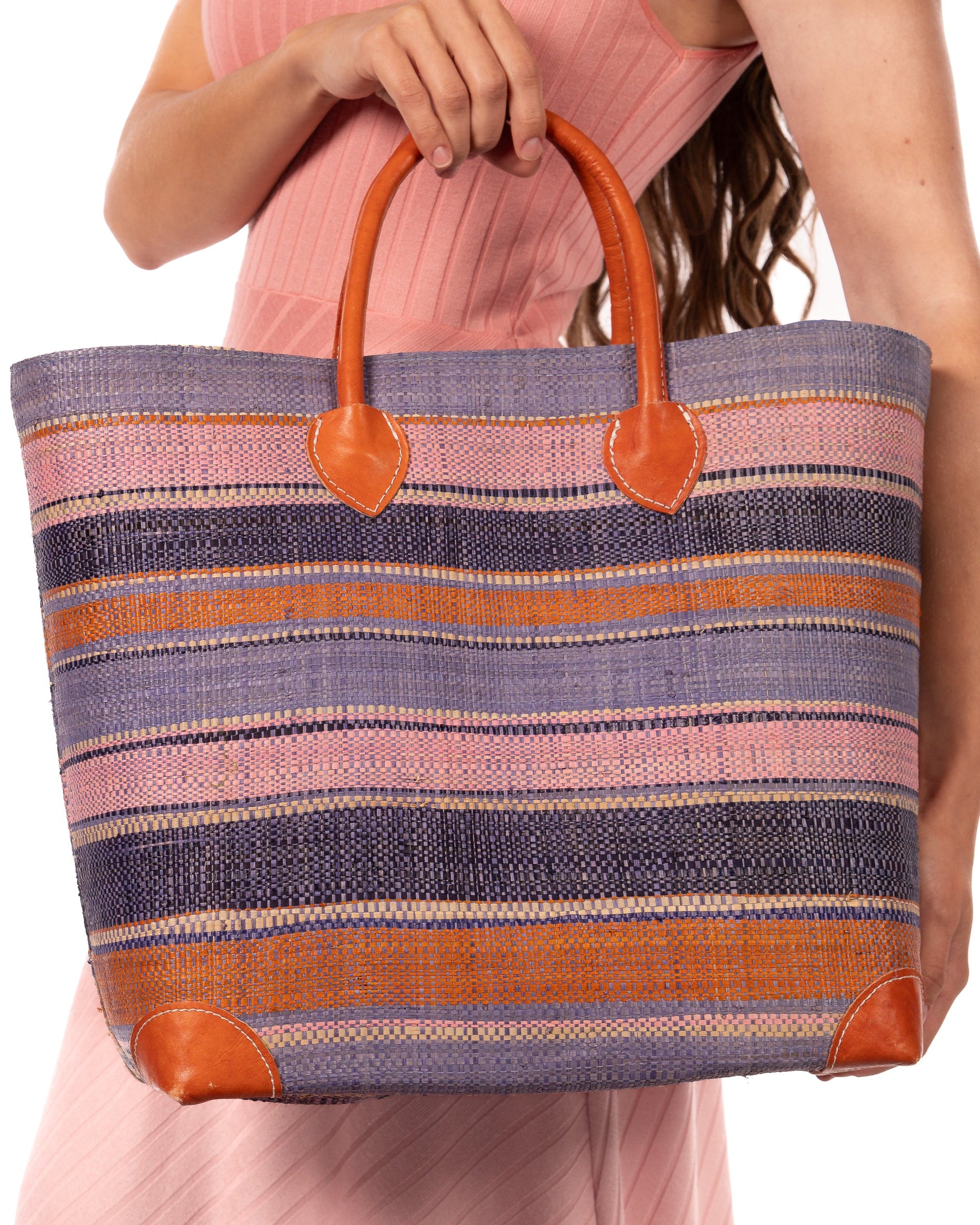Model Wearing Rayo Stripes Straw Basket Bag Retro Stripe handmade loomed natural raffia palm fiber in a horizontal stripe pattern of multiple widths of natural straw color, denim/retro/light blue, navy/dark blue, baby pink, coral orange/red, etc. handbag with leather handles tote beach bag - Shebobo