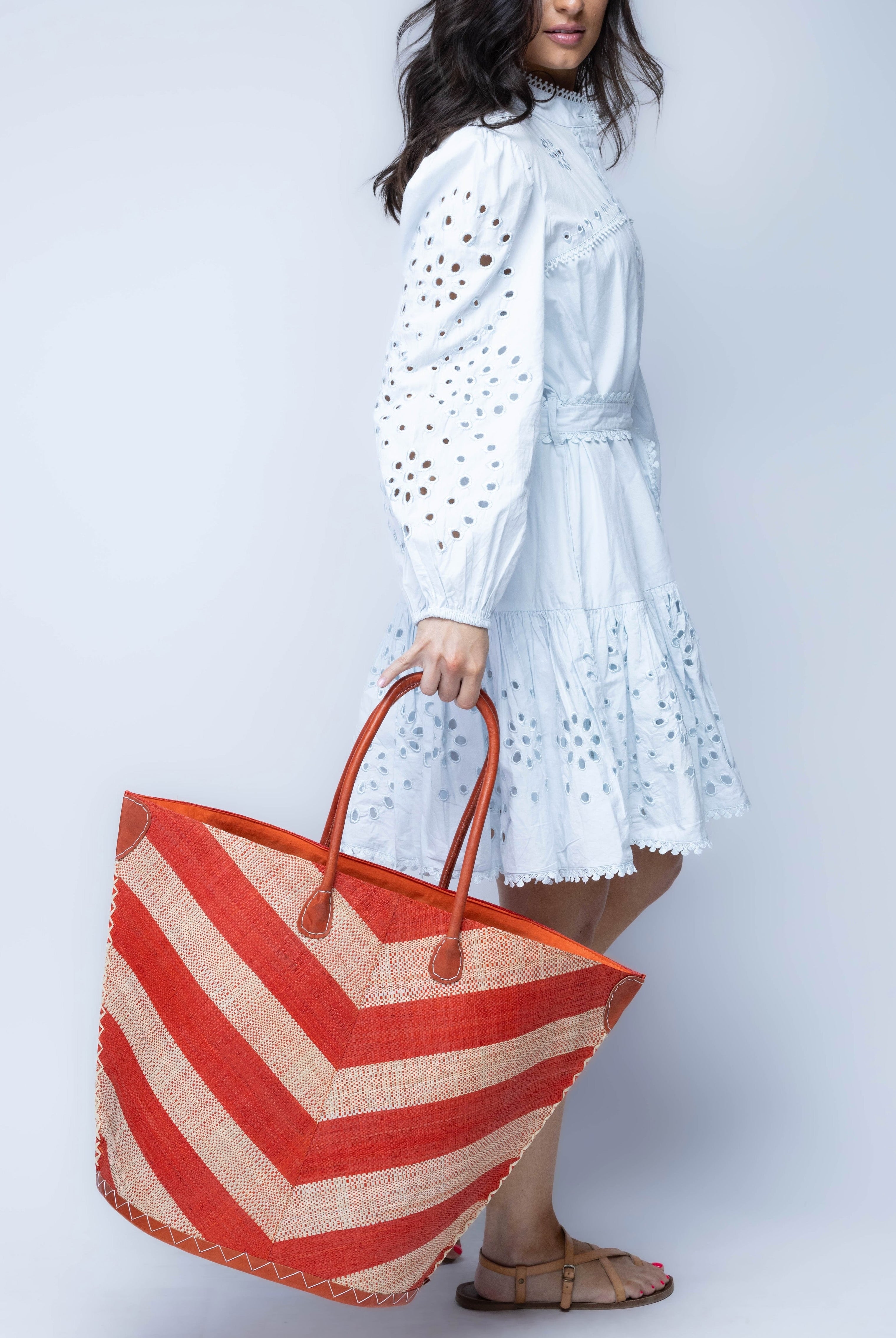 Model wearing Santa Cruz Wide Stripe Chevron Large Straw Tote Bag handmade loomed raffia palm fiber in a two tone diagonal even width bands of color in a wide stripe chevron pattern of coral orange/red and natural straw color on the front and a matching solid hue on the back with leather accents and handles large shoulder bag - Shebobo