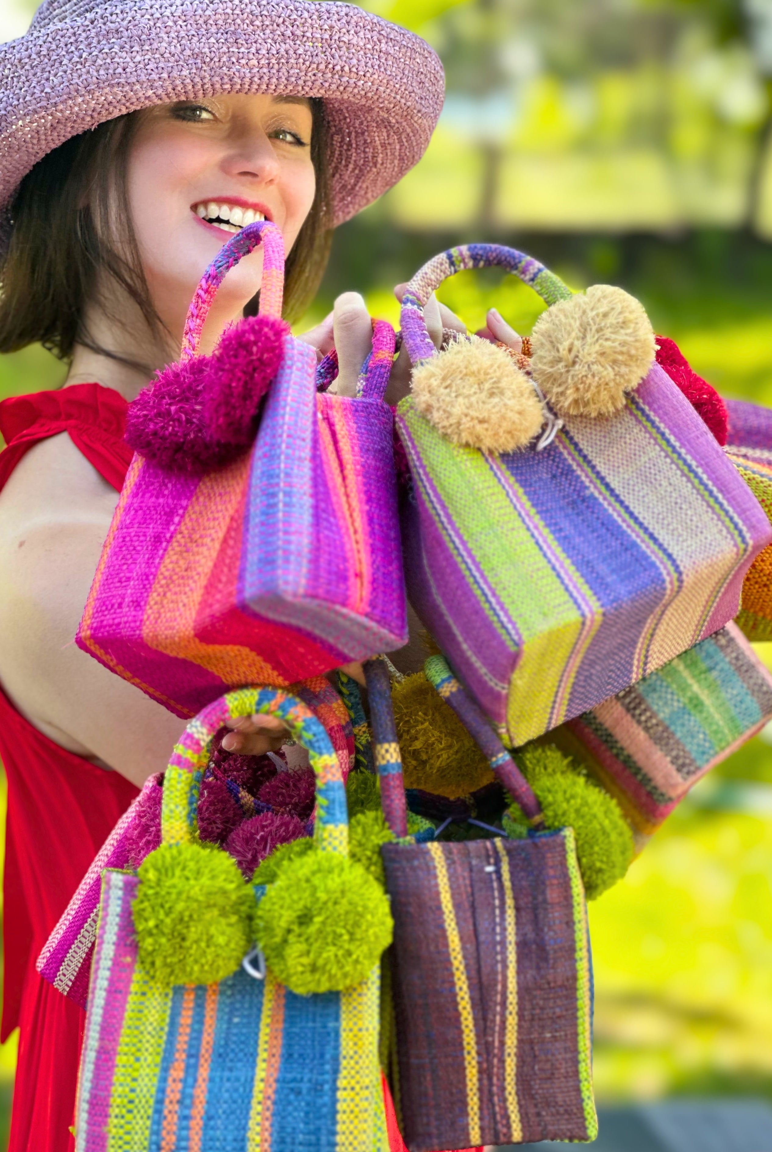 Model wearing Schooner Straw Mini Bag with Pompom Accent Variety of Colorways handmade loomed raffia palm fiber in multicolor vertical stripe patterns with matching raffia pouf details extra small handbag purse with 3" Brim Leor Lilac purple Crochet Raffia Straw Sun Hat - Shebobo
