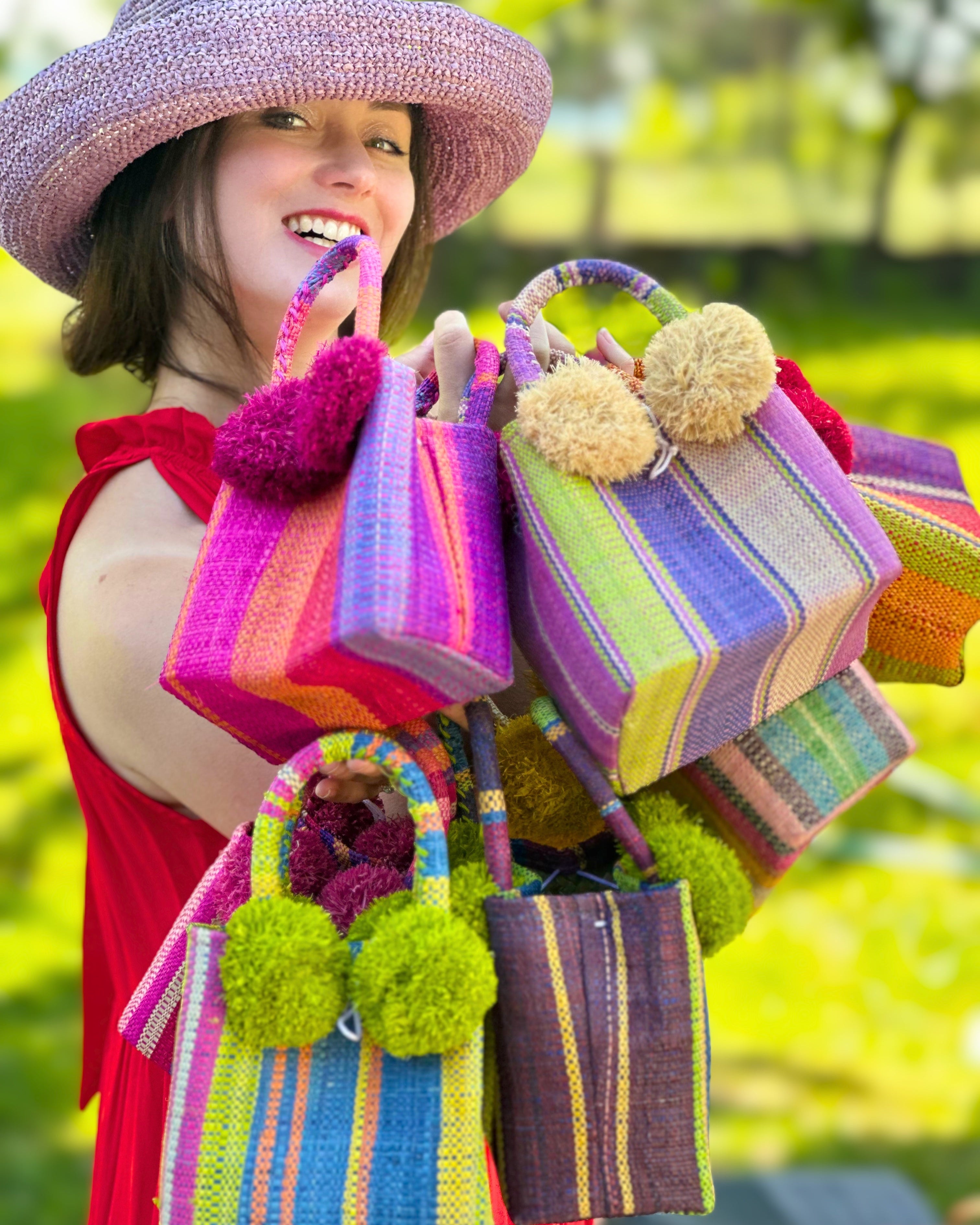 Model wearing Schooner Straw Mini Bag with Pompom Accent Variety of Colorways handmade loomed raffia palm fiber in multicolor vertical stripe patterns with matching raffia pouf details extra small handbag purse with 3" Brim Leor Lilac purple Crochet Raffia Straw Sun Hat - Shebobo