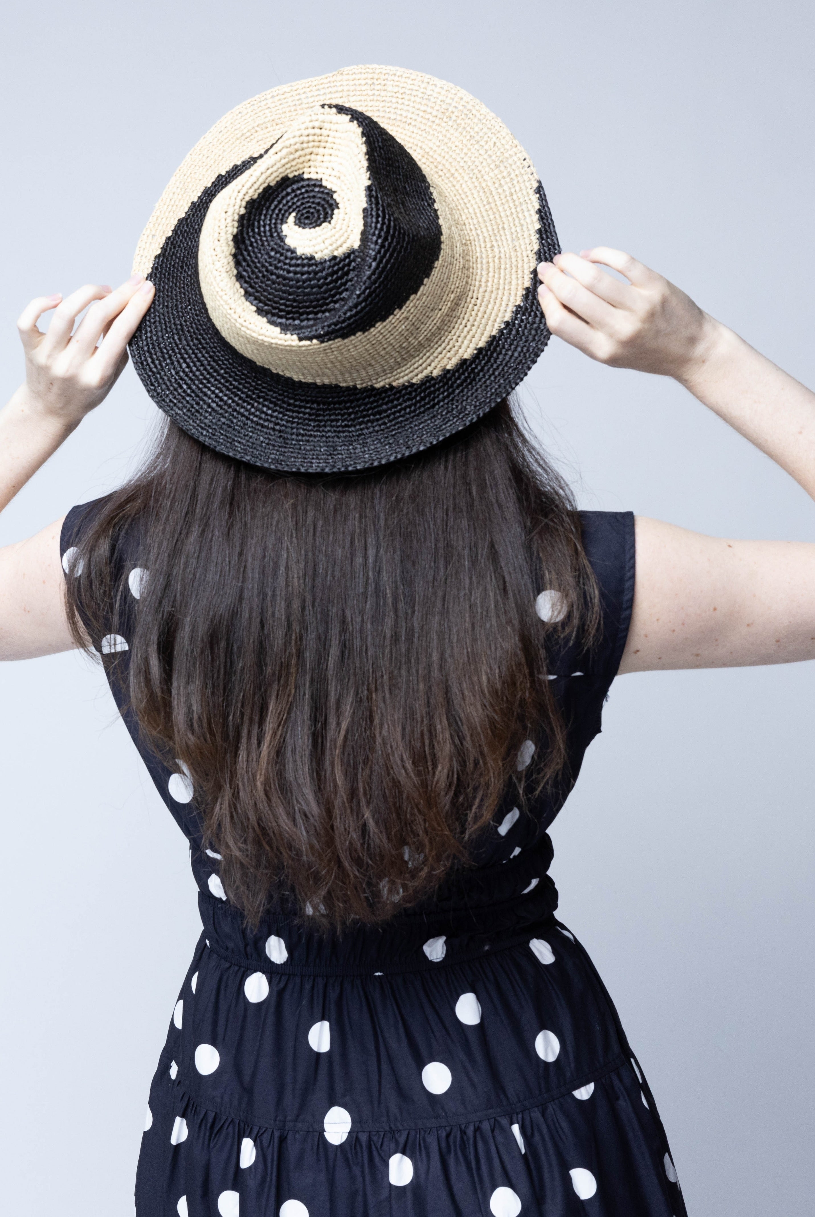 Model wearing Sequoia Black and Natural 3" Brim Swirl Crochet Panama Unisex Straw Hats handmade crochet natural raffia palm fiber in a two tone color swirl design of black and natural straw color spiraling together from wide bands around the brim to a narrow twist at the top of the crown - Shebobo