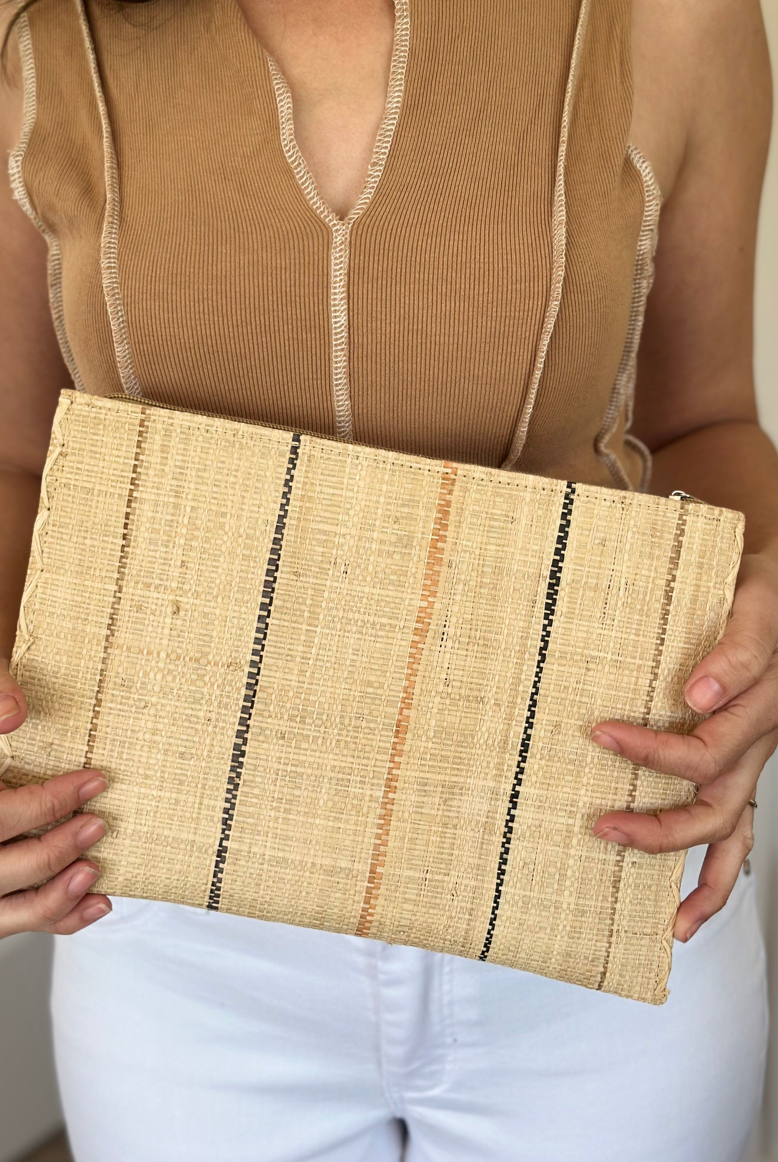 Model wearing Set of 3 Neutrals on Natural straw color Nesting Zippered Straw Clutches Pinstripe Pattern handmade loomed raffia in wide vertical bands of natural with multicolor narrow bands of cinnamon/tobacco/brown, black, and blush with matching zipper and braided zipper pull with cross stitch edging in three sizes of small, medium, and large - Shebobo