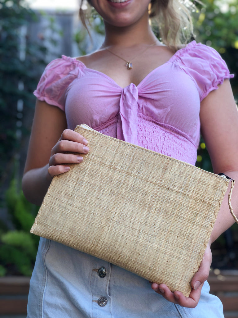 Model wearing size large of Set of 3 Natural straw color Nesting Zippered Straw Clutches Solid Colors handmade loomed raffia in a solid hue with matching zipper and braided zipper pull with cross stitch edging in three sizes of small, medium, and large - Shebobo