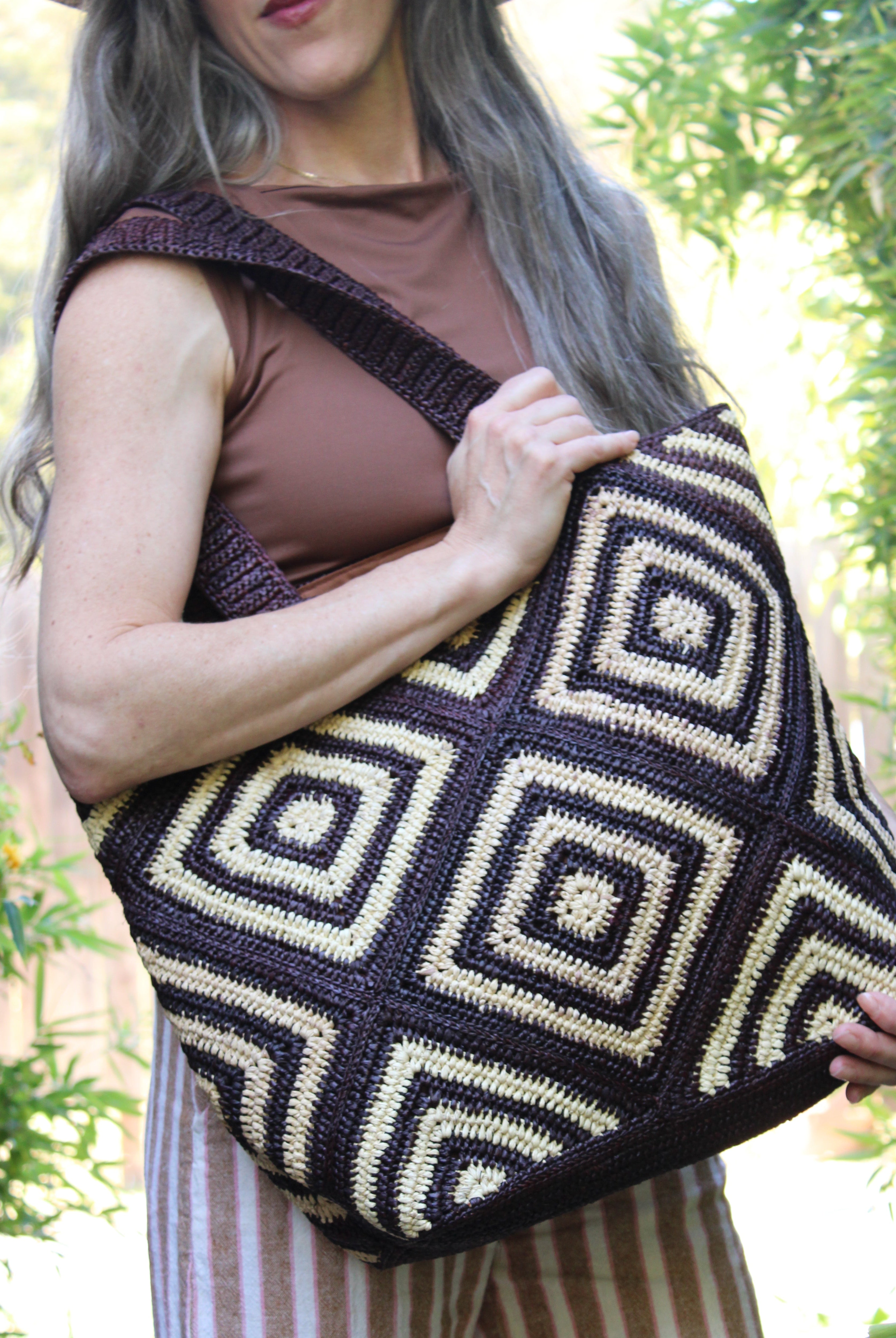 Model wearing Seychelle Mocha and Natural Diamond Pattern Crochet Straw Basket Handbag handmade natural raffia palm fiber in a two tone multicolor geometric diamond pattern with aternating Mocha chocolate/dark/brown and natural straw colored diamonds that make a diagonal bullseye pattern with matching crochet handles beach bag tote purse - Shebobo