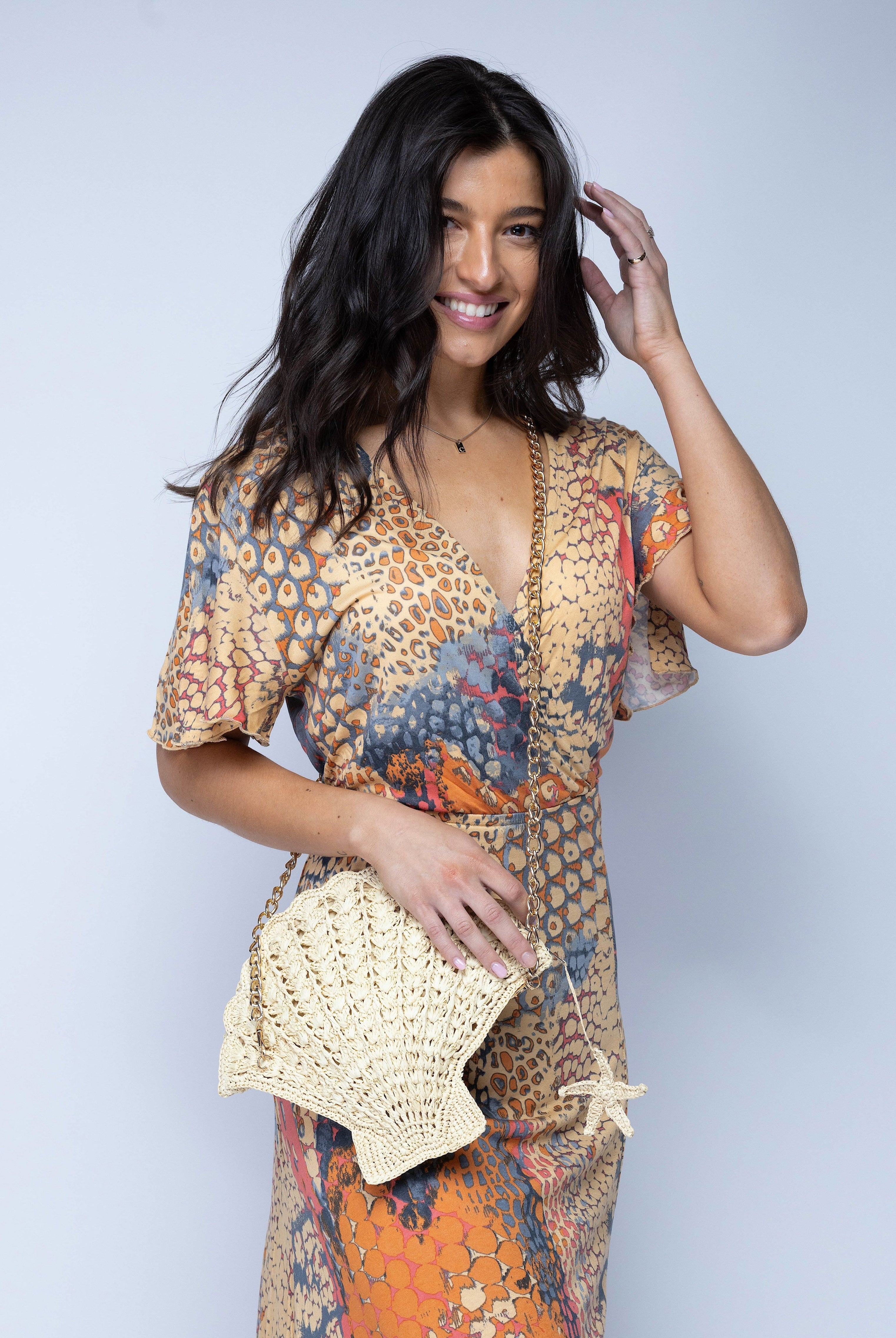 Model wearing Shelly Seashell Crochet Straw Crossbody Bag handmade natural raffia palm fiber in a solid hue of natural straw color crochet into the shape of a seashell with detailed texture representing the shell shape with metal chain crossbody strap and natural small starfish zipper pull charm embellishment purse beach bag - Shebobo