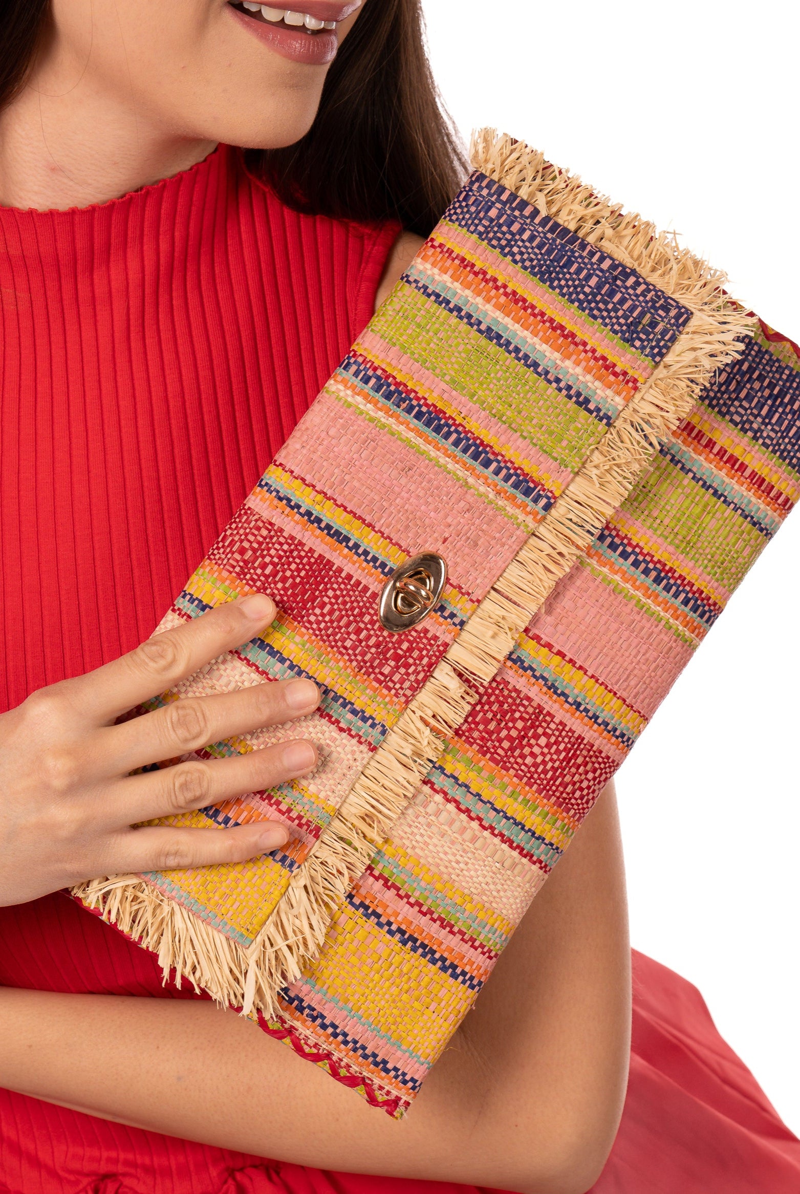 Model wearing Sophie Raspberry Swirl Multicolor Stripes Straw Clutch handmade loomed raffia purse handbag in muti-width vertical bands of pink, yellow, purple, blue, orange, cappuccino light brown, and natural straw color with matching cross stitch edging and natural straw color raw fringe edge envelope shaped bag - Shebobo
