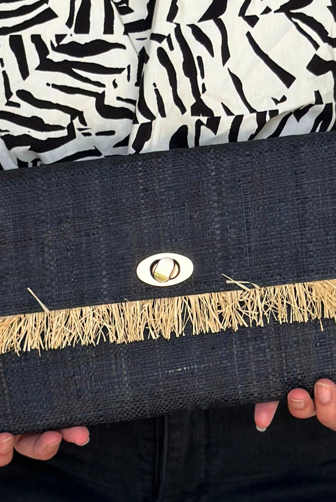 Model wearing Sophie Black Straw Clutch with Raw Fringe Edge handmade loomed black raffia purse with contrasting natural straw color fringe trim edge and matching cross stitch binding handbag - Shebobo