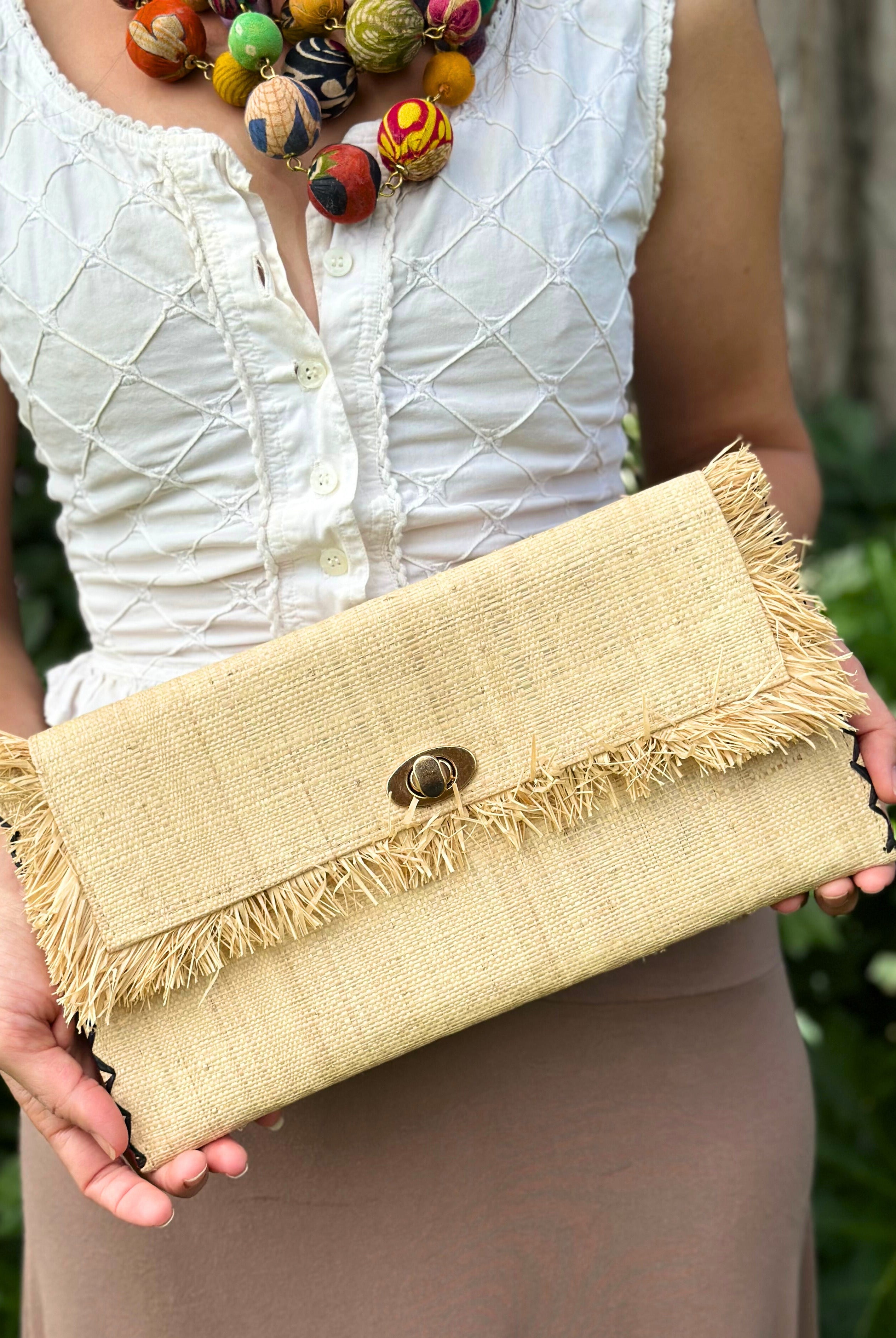 Model wearing Sophie Natural Straw Clutch with Raw Fringe Edge handmade loomed natural straw color raffia purse with matching fringe trim edge and contrasting black cross stitch binding handbag - Shebobo