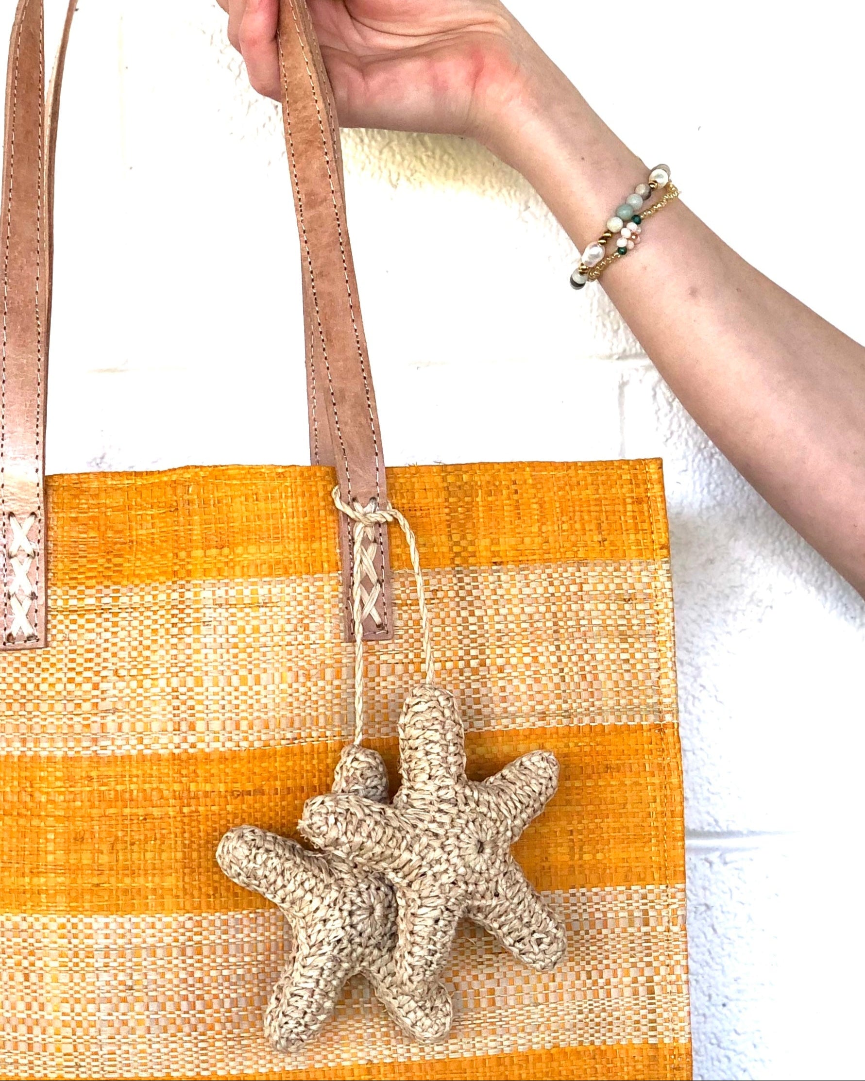 Model wearing Starfish Tie Crochet Raffia Charm Embellishment handmade natural raffia palm fiber is crochet into 3D starfish shapes in natural straw color and connected with raffia twist tie beach bag embellishment - Shebobo