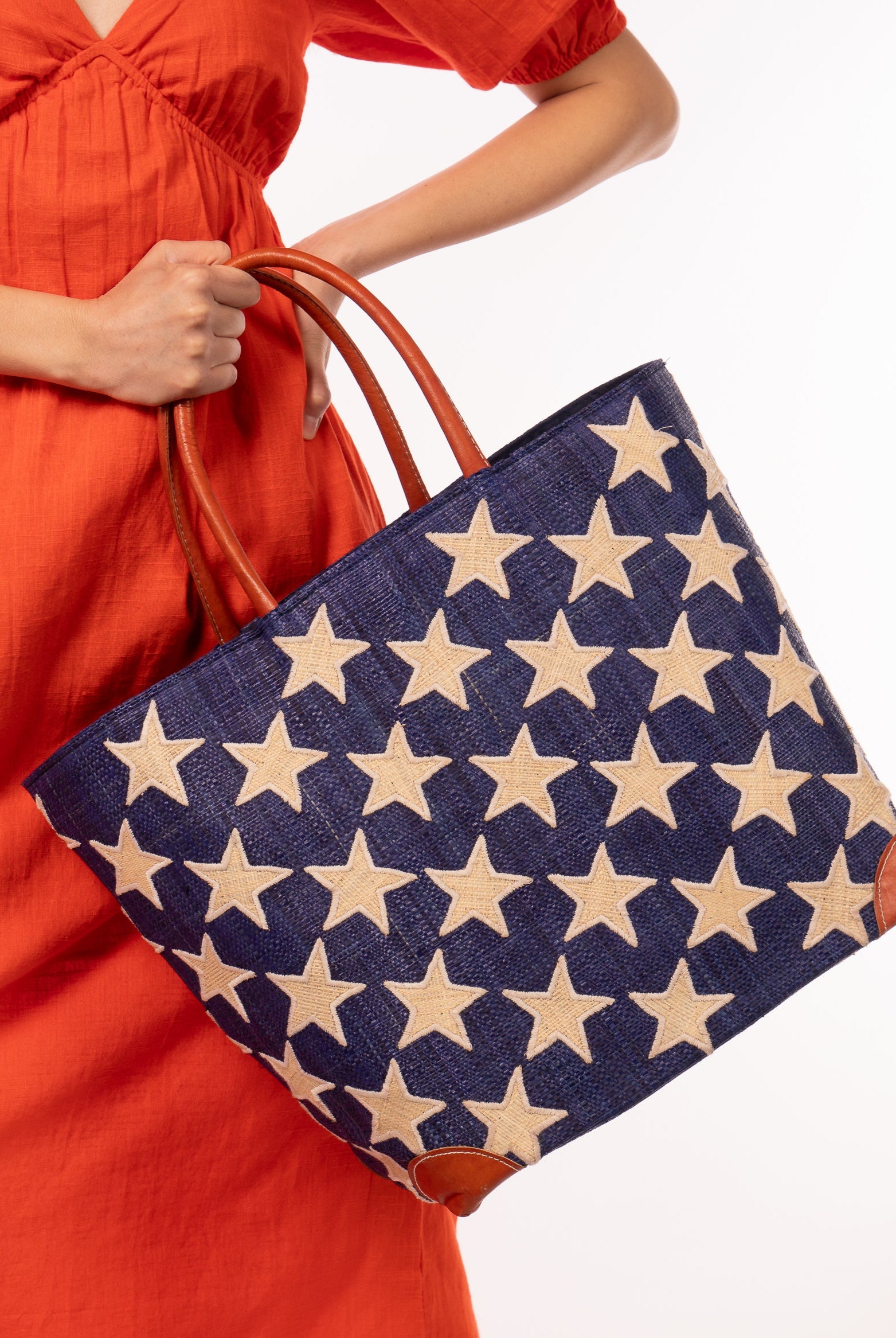 Model wearing Stars Straw Basket Bag handmade loomed raffia palm fiber in a solid hue of Dusk navy/dark/blue with natural straw color loomed stars stitched on in a tight diagonal pattern with leather handles Patriotic Americana Shoulder Bag Beach Bag - Shebobo