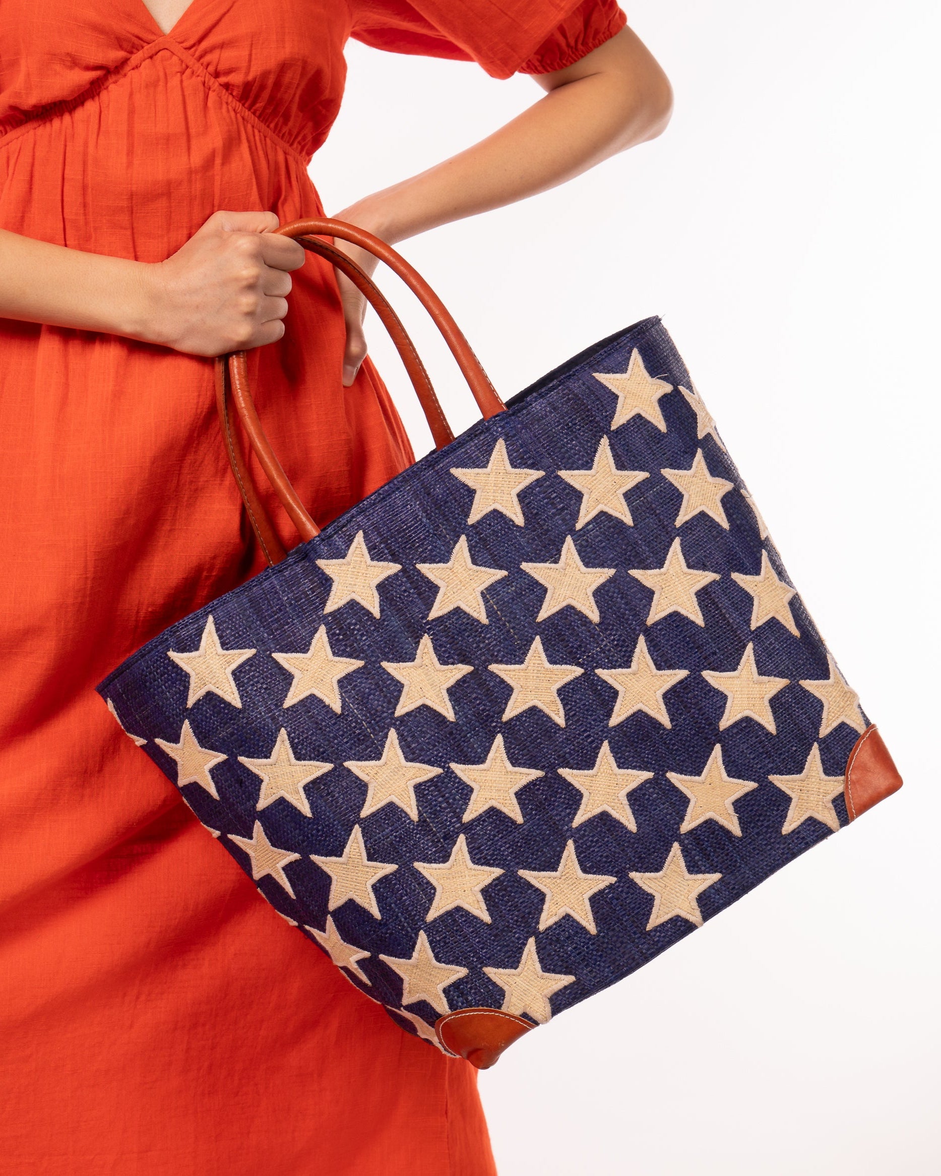Model wearing Stars Straw Basket Bag handmade loomed raffia palm fiber in a solid hue of Dusk navy/dark/blue with natural straw color loomed stars stitched on in a tight diagonal pattern with leather handles Patriotic Americana Shoulder Bag Beach Bag - Shebobo
