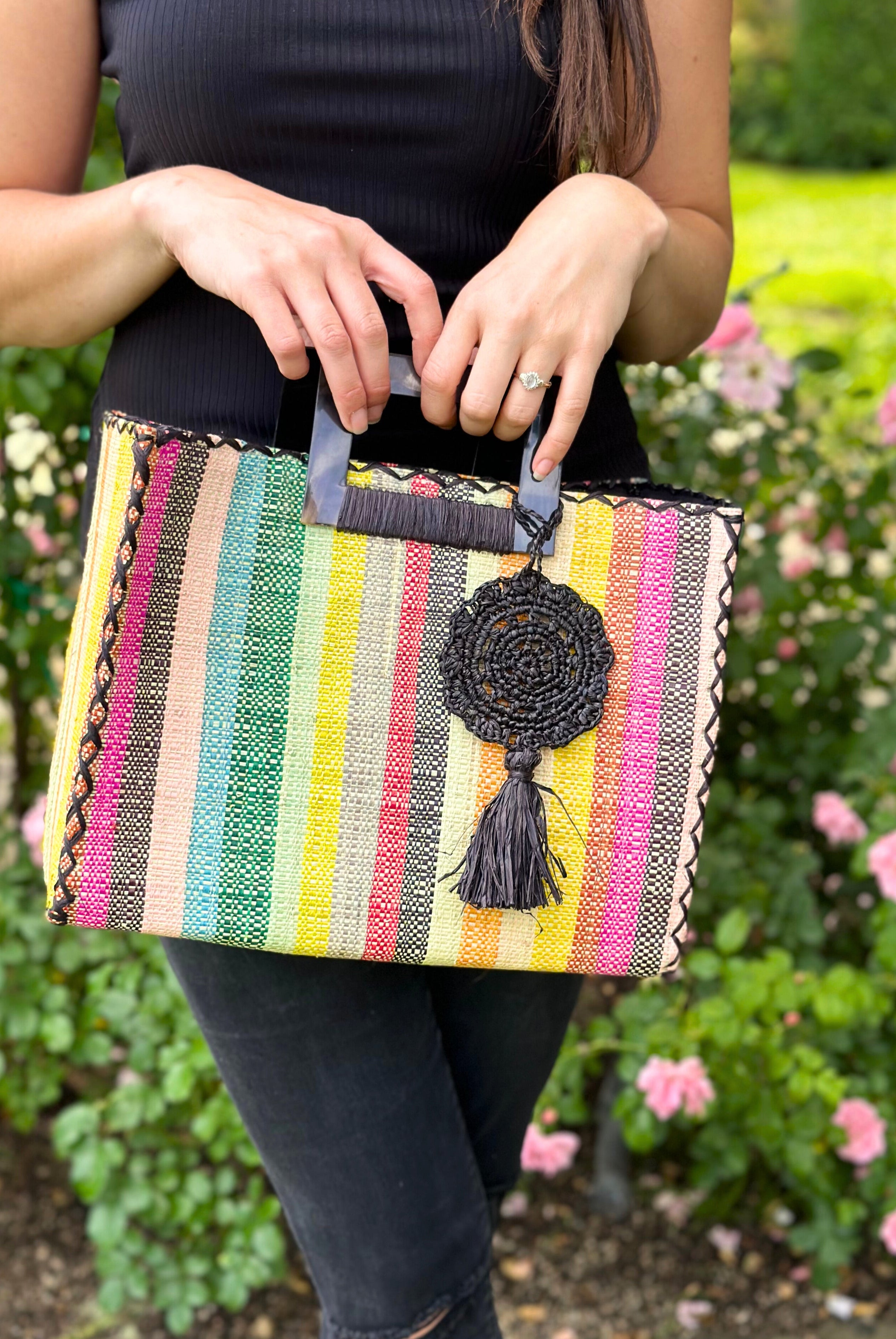 Model wearing Stevie Square Lollipop Multicolor Stripe Straw Handbag with Horn Handles handmade loomed raffia with yellow, saffron, light blue, green, red, black, fuchsia, orange, natural, etc. varying width vertical stripe pattern purse with matching black liner, cross stitch edging, and handle attachment - Shebobo