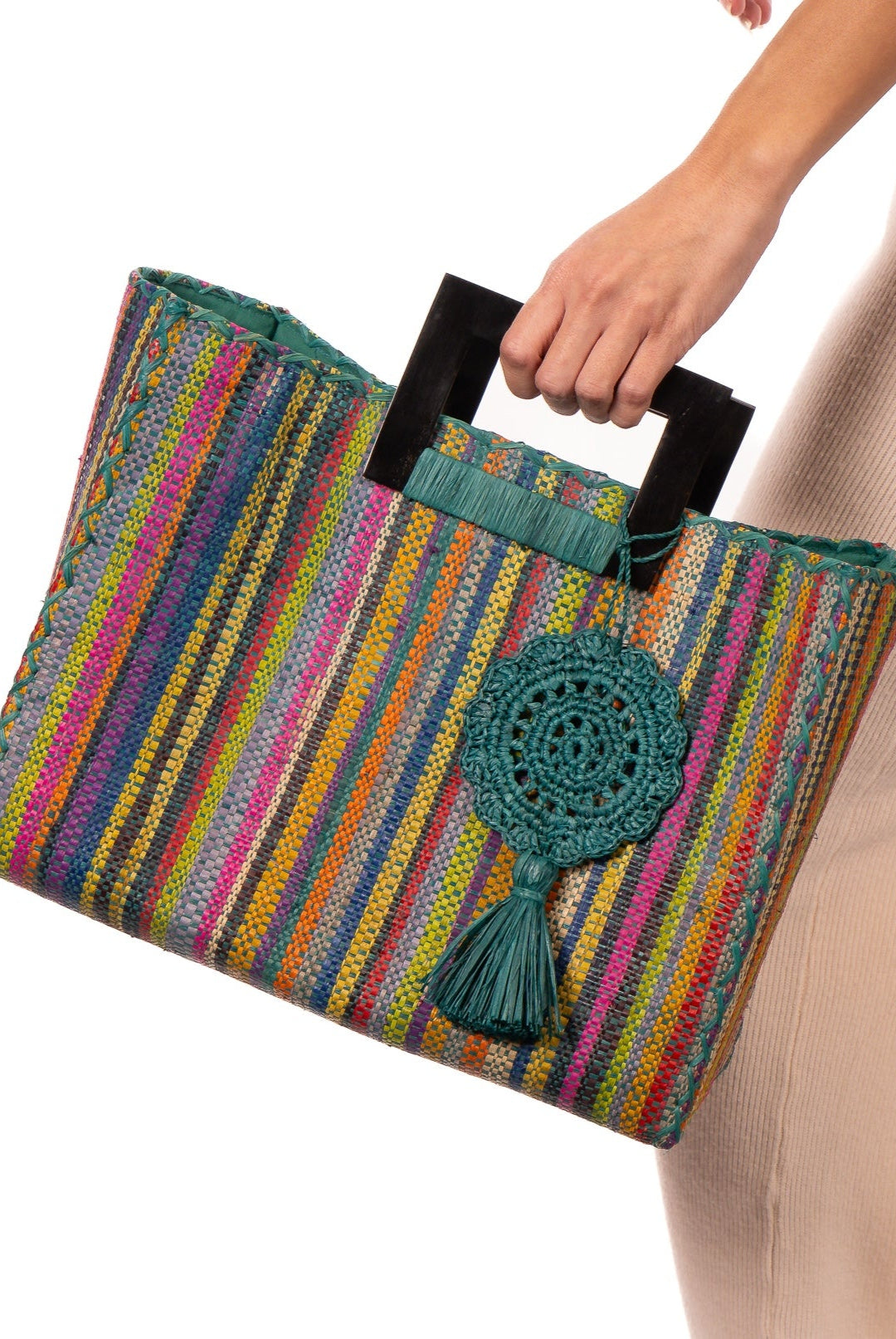 Model wearing Stevie Square Turquoise Stripes Multicolor Straw Handbag with Horn Handles handmade loomed raffia with turquoise, navy, light blue, purple, red, black, fuchsia, orange, yellow, lime, etc. varying width vertical stripe pattern purse with matching turquoise liner, cross stitch edging, handle attachment, and crochet doily tassel embellishment - Shebobo