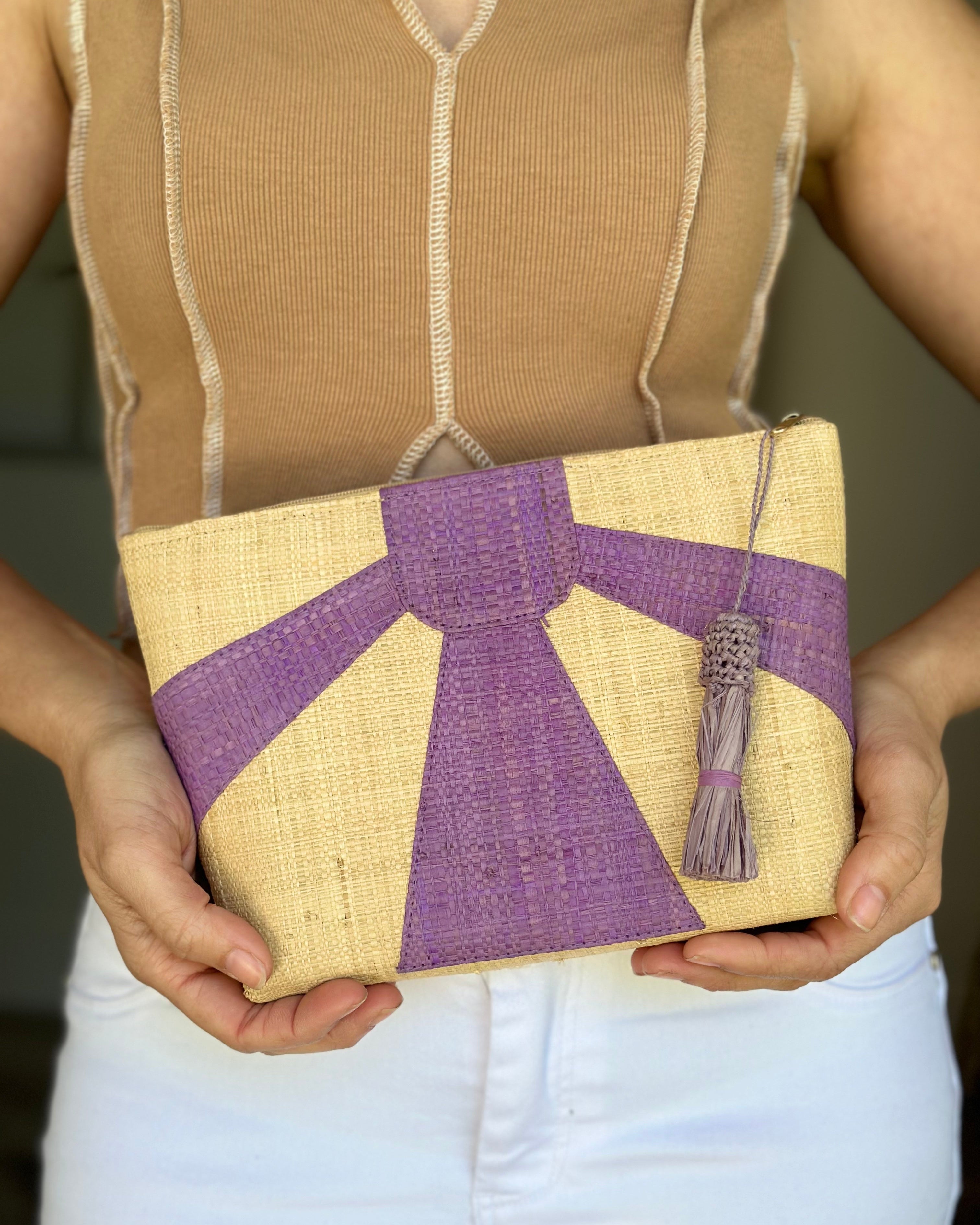 Model wearing Sunburst Cosmetic Clutch with Tassel Zipper Pull handmade zippered pouch purse with sunburst pattern of amethyst/lavender blue/purple on natural loomed raffia palm fibers and matching colored tassel pull handbag - Shebobo