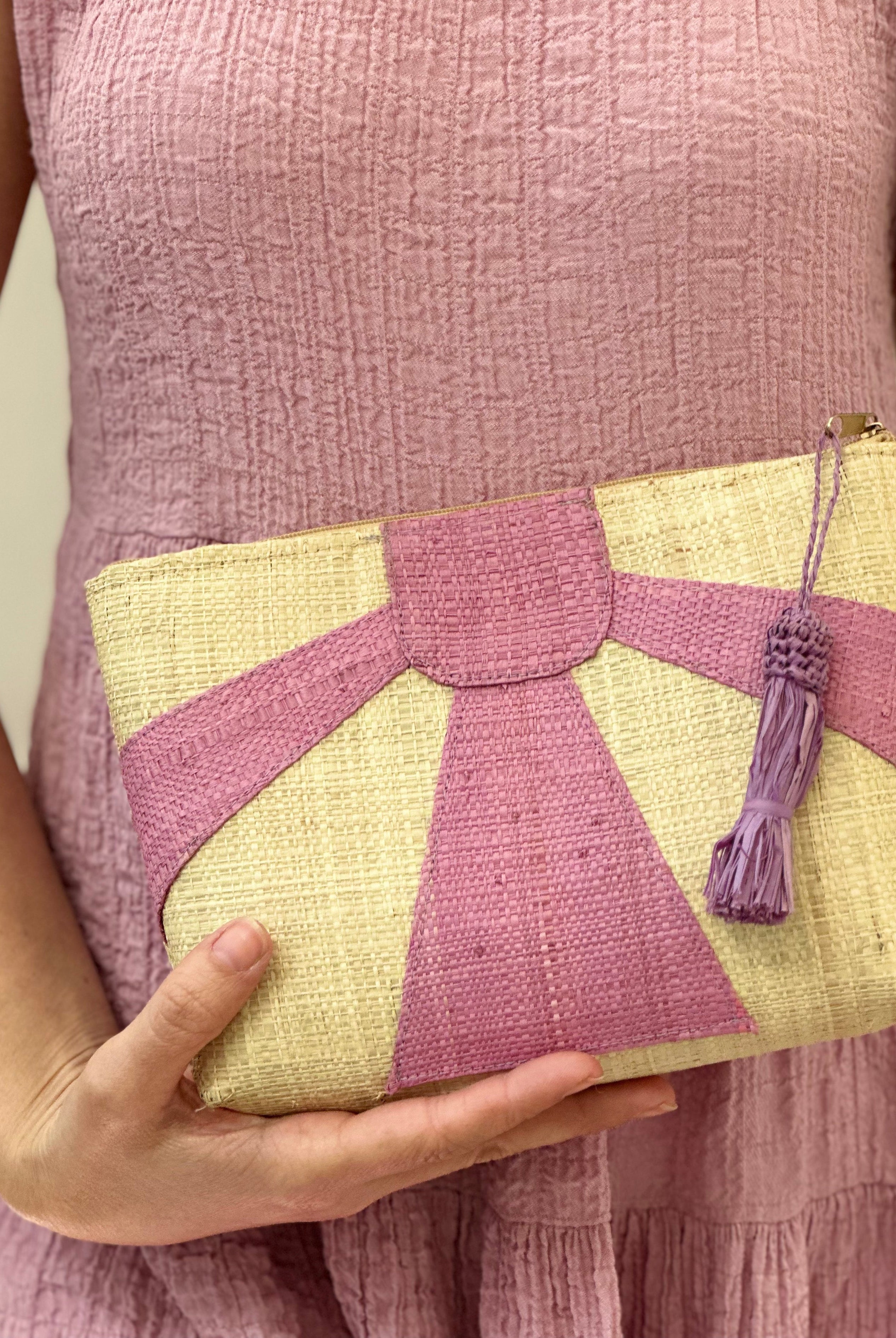 Model wearing Sunburst Cosmetic Clutch with Tassel Zipper Pull handmade zippered pouch purse with sunburst pattern of wisteria/lavender/lilac pink/purple on natural loomed raffia palm fibers and matching colored tassel pull handbag - Shebobo