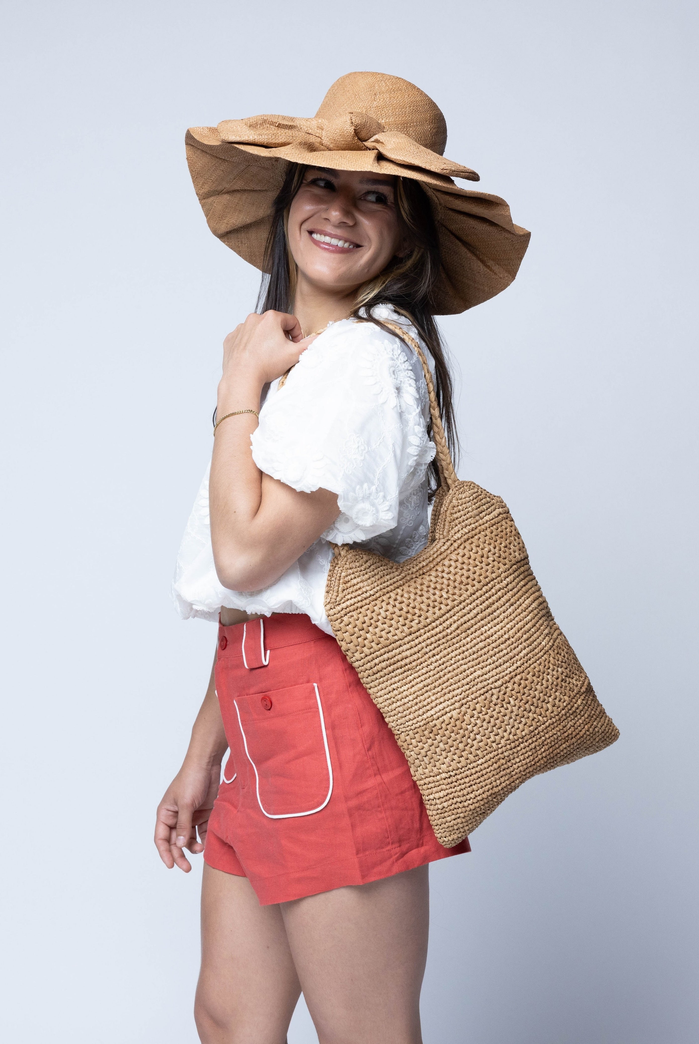 Model wearing Tiana Crochet Straw Shoulder Bag Purse handmade crochet natural raffia palm fiber in a solid hue of Cappuccino tea/light/brown in subtle textured horizontal bands of two link patterns with matching braided handles - Shebobo (with Lilly 5" Brim Fan Pleated Straw Sun Hats with Big Bow)