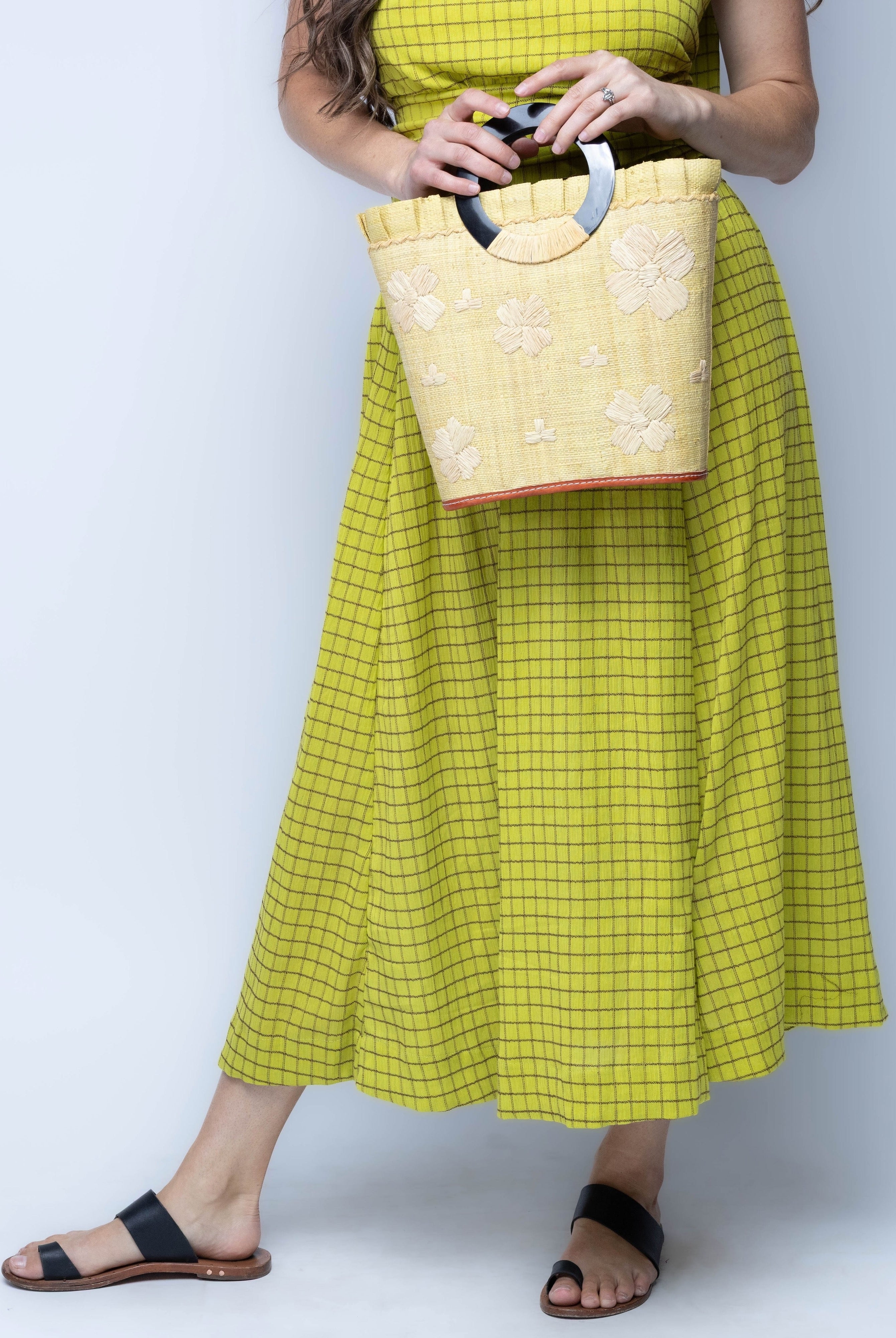 Model wearing Tulum Straw Bucket Bag with Flower Embroidery and Horn Handle Butter Purse with Ruffle Edge handmade loomed raffia palm fiber in a solid hue of butter light/yellow with natural straw color hand embroidered floral pattern with multiple sized flowers and raffia ruffle on the opening handbag - Shebobo