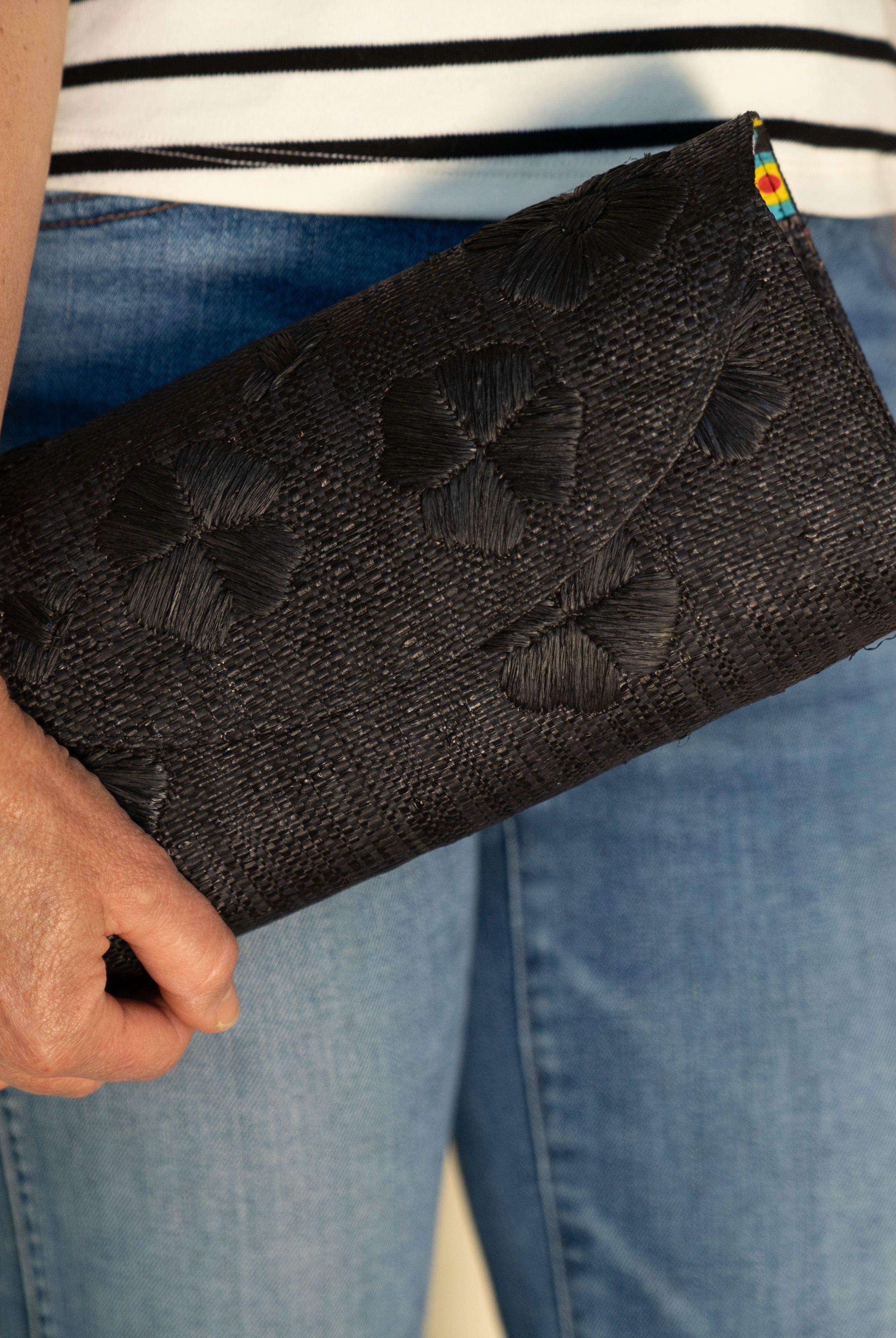 Model wearing Tulum Clutch Black Flower Embroidery handmade loomed raffia palm fibers with envelope clutch shape, embroidered multi-sized embroidered flower pattern, and assorted interior wax cloth African Print liners plus zippered pocket - Shebobo