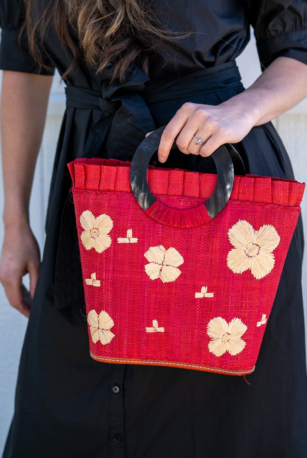Model wearing Tulum Straw Bucket Bag with Flower Embroidery and Horn Handle Red Purse with Ruffle Edge handmade loomed raffia palm fiber in a solid hue of red with natural straw color hand embroidered floral pattern with multiple sized flowers and raffia ruffle on the opening handbag - Shebobo