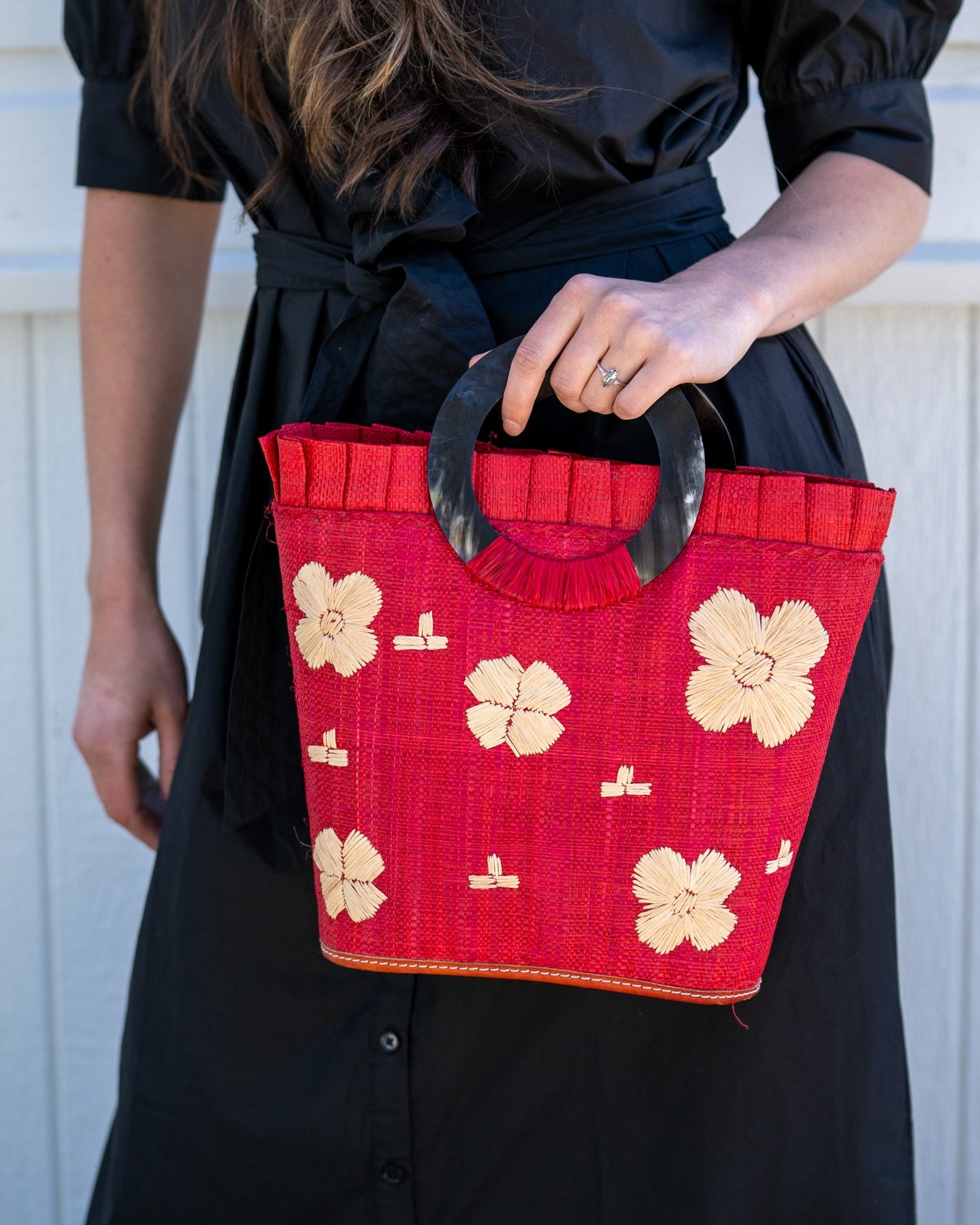 Model wearing Tulum Straw Bucket Bag with Flower Embroidery and Horn Handle Red Purse with Ruffle Edge handmade loomed raffia palm fiber in a solid hue of red with natural straw color hand embroidered floral pattern with multiple sized flowers and raffia ruffle on the opening handbag - Shebobo