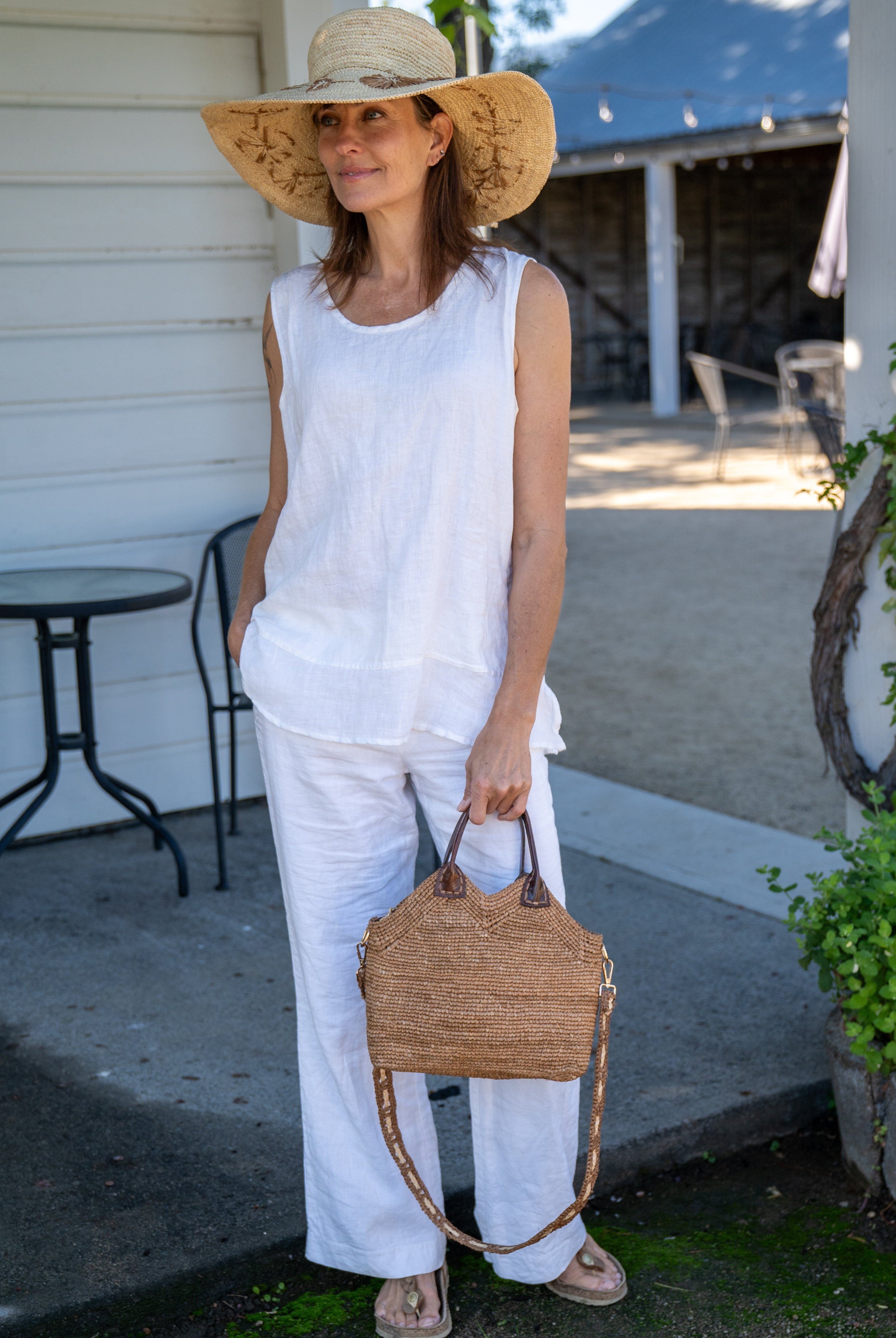 Model wearing Victoria Crochet Straw Handbag Convertible Crossbody Bag handmade crochet natural raffia palm fiber in a solid hue of cappuccino tea/light/brown in a subtle texture of horizontal link bands pattern across the bag and m shape around the top of the bag with dark brown leather handles and removable two tone natural and cappuccino tea/light/brown crossbody strap convertible purse - Shebobo (with Gigi 5.5" Brim Floral Embroidered Crochet Straw Sun Hats)