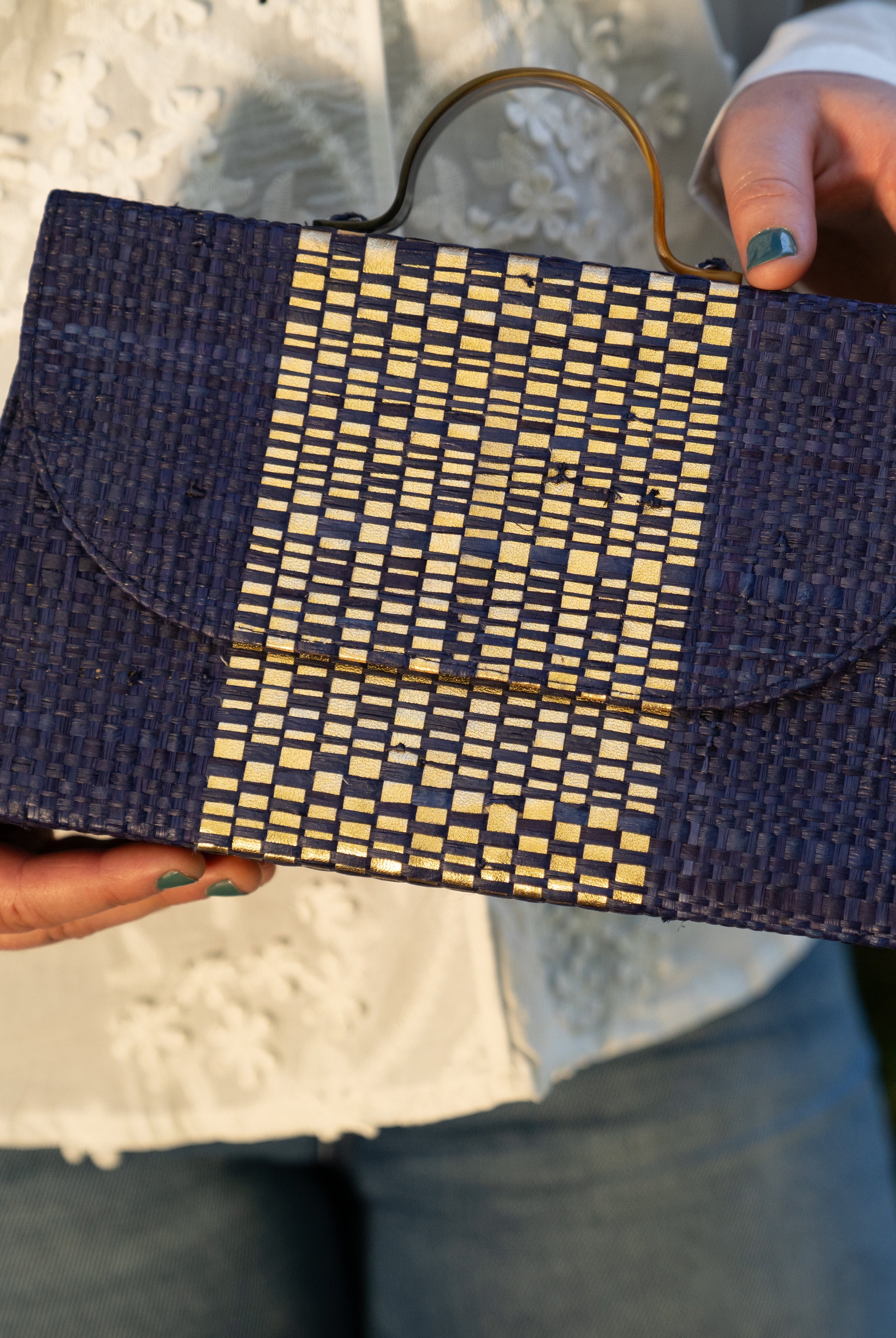 Model wearing Wynwood Navy Straw Handbag with Metallic Detailing & Horn Handle handmade loomed raffia in navy blue and silver metallic vegan leather in three vertical bands of color with the metallic weave centered on the purse under the handles - Shebobo