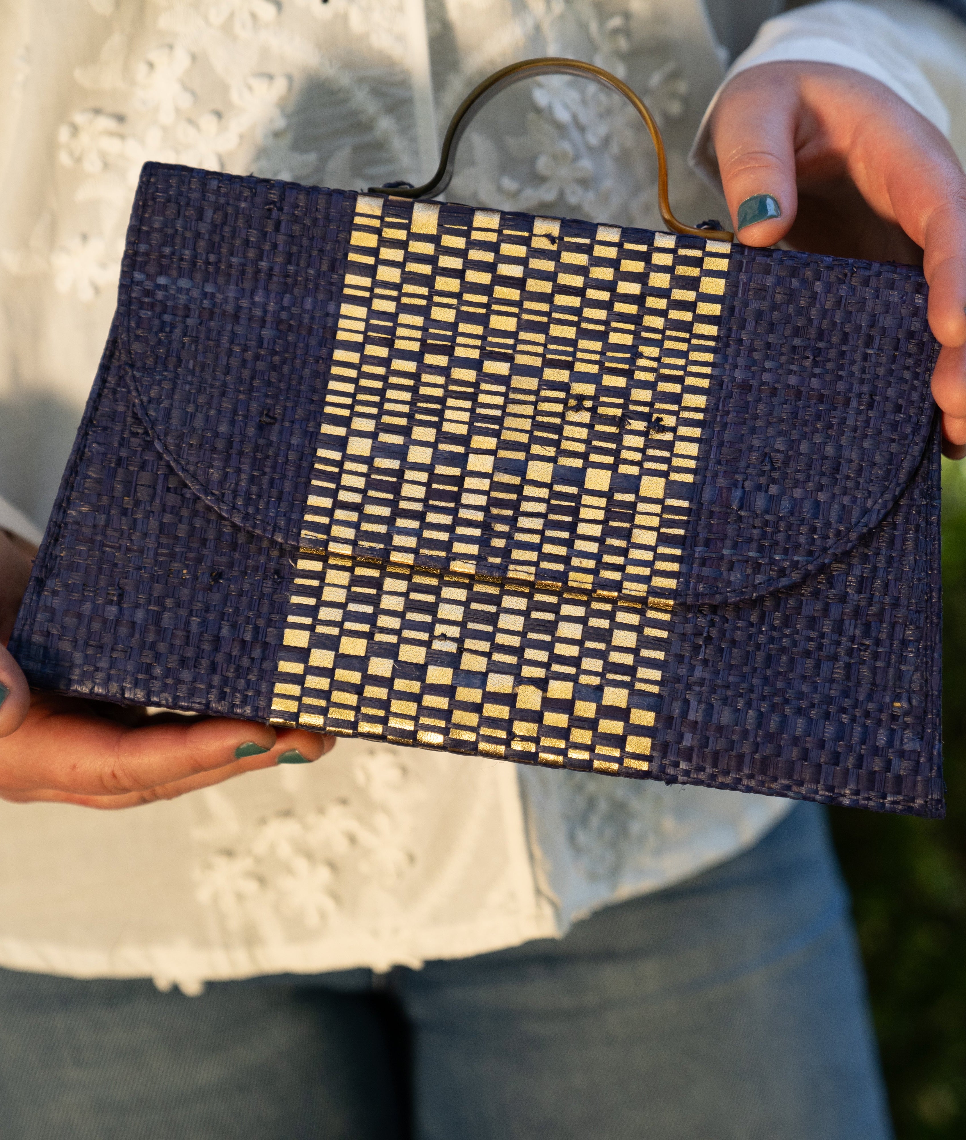 Model wearing Wynwood Navy Straw Handbag with Metallic Detailing & Horn Handle handmade loomed raffia in navy blue and silver metallic vegan leather in three vertical bands of color with the metallic weave centered on the purse under the handles - Shebobo