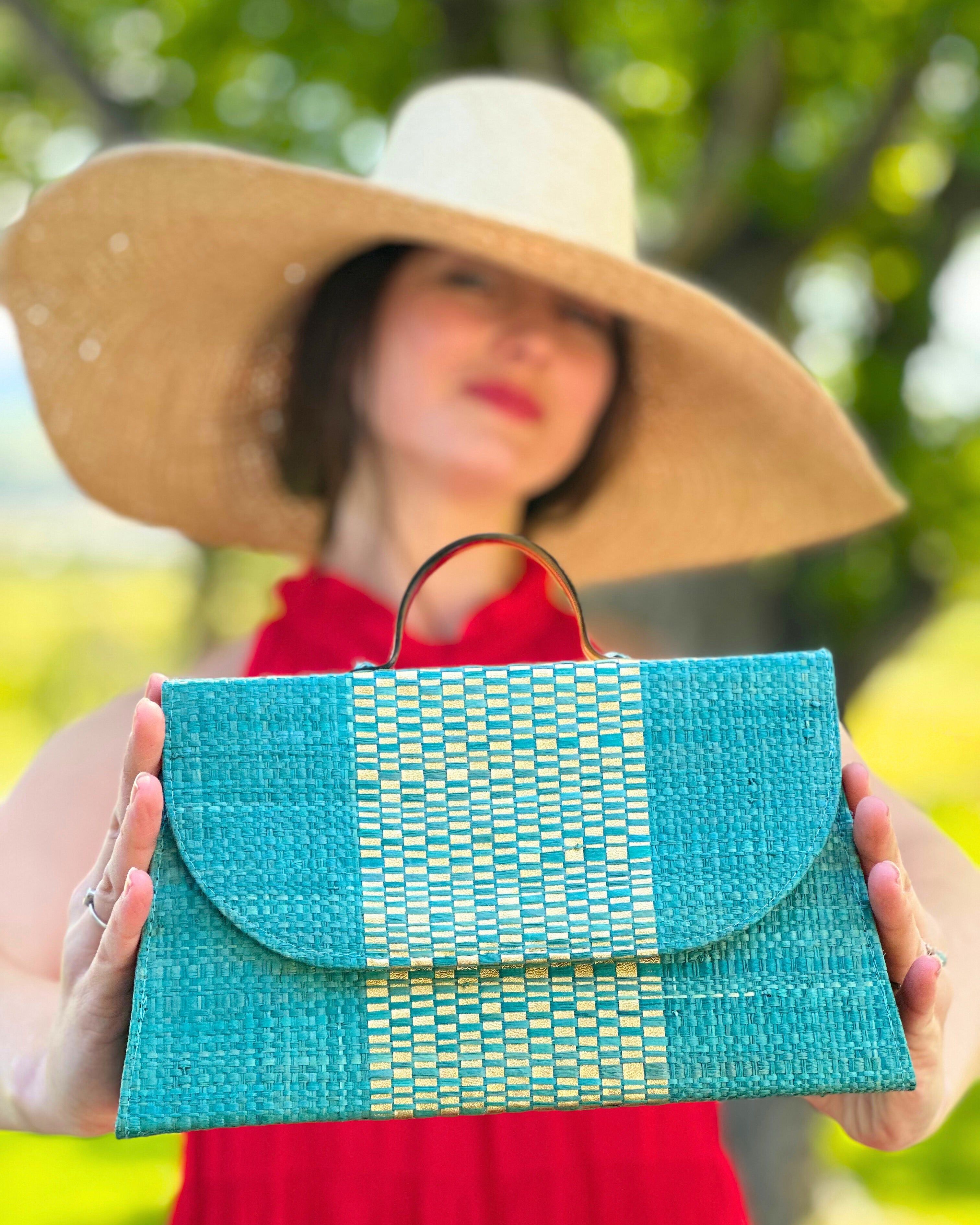 Model wearing Wynwood Turquoise Straw Handbag with Metallic Detailing & Horn Handle handmade loomed raffia in turquoise blue and metallic vegan leather in three vertical bands of color with the metallic weave centered on the purse under the handles with 7" Wide Brim Natasha Natural Woven Straw Sun Hat - Shebobo