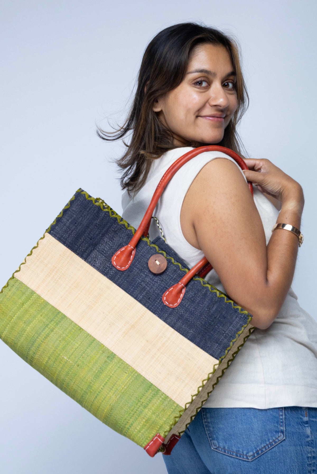 Model wearing Zafran 3 Tone Color Block Beach Straw Bag with Plastic Liner handmade loomed raffia palm fiber in three equally sized horizontal bands of black, natural straw color, and martini olive/dark/green with wood button and leather handles - Shebobo