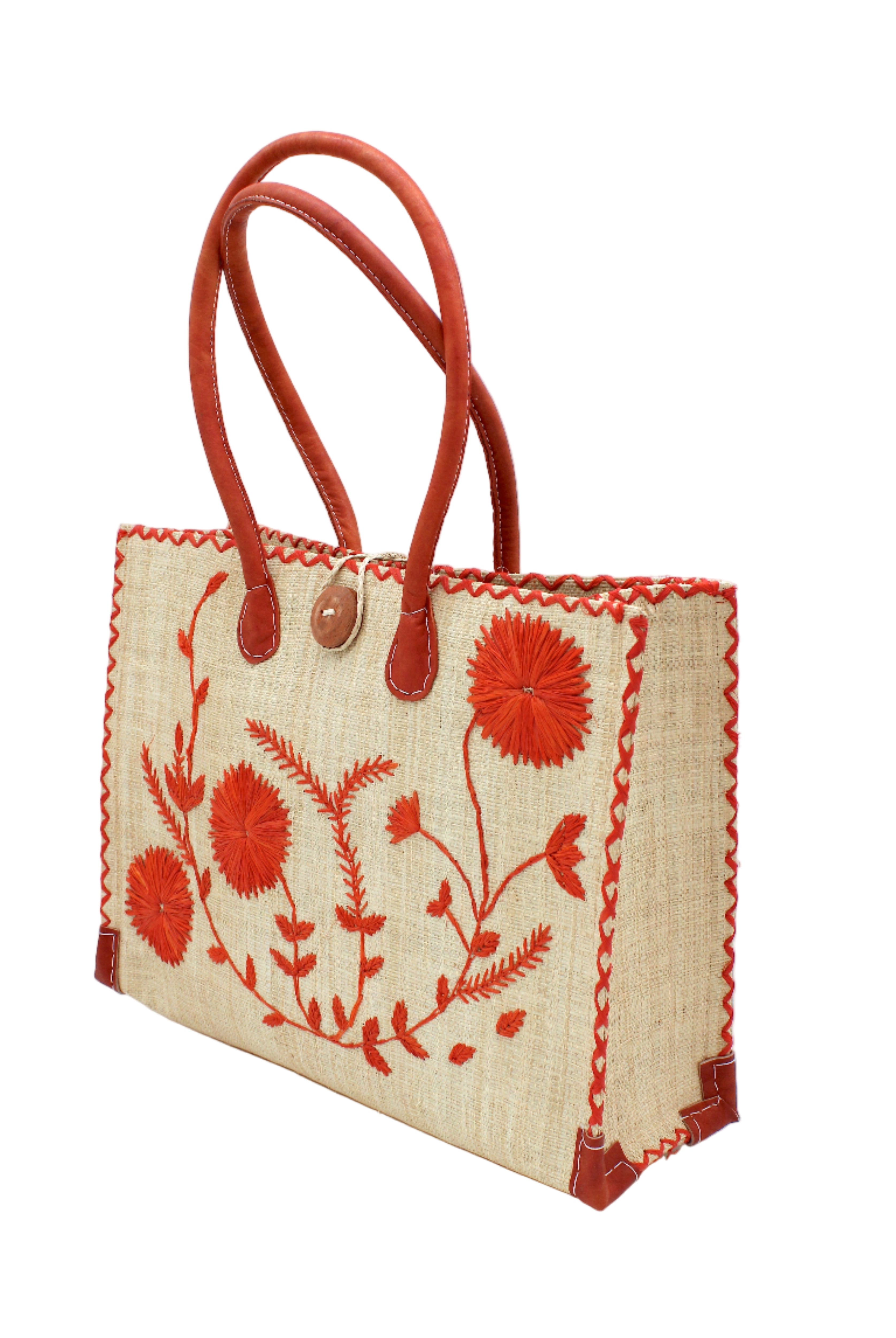 Side view Zafran Natural & Coral Embroidered Straw Beach Bag with Floral Pattern handmade natural raffia palm fiber in a solid hue of natural straw color with asymmetrical floral leaf, vine, and flower pattern in coral orange/red with matching cross-stitch edging, leather handles, and wooden button closure shoulder bag handbag tote - Shebobo