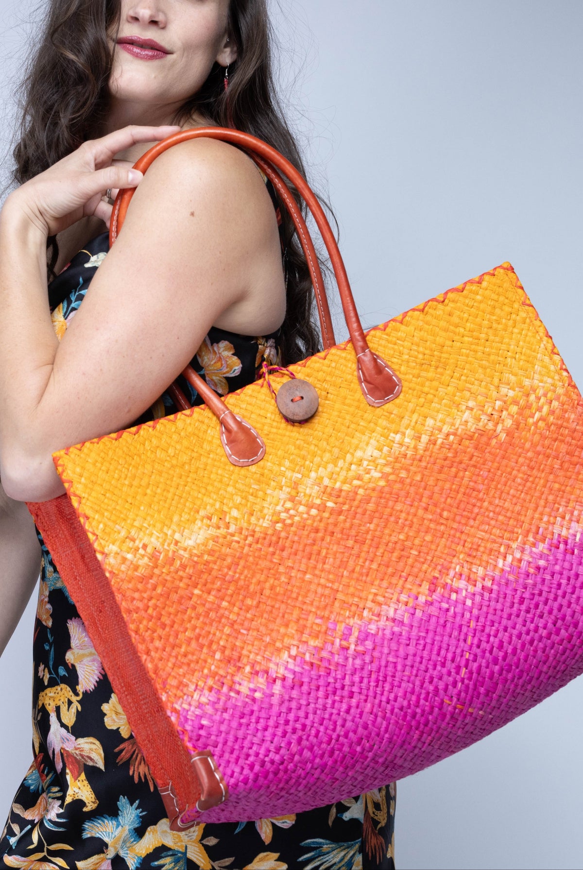 Model wearing Holden Fuchsia Ombre Zafran Straw Beach Bags handmade dip dyed raffia woven into a three part horizontal ombre pattern of coral orange/red, fuchsia pink, and saffron yellow with cross stitch edging, wooden button, and leather handles - Shebobo