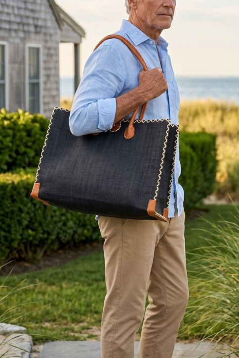 Model wearing Zafran Straw Beach Bag with Plastic Liner handmade loomed raffia in a solid hue of black with contrasting natural straw color cross stitch edge binding, wood button closure, and leather handles & feet plus assorted print plastic lining - Shebobo
