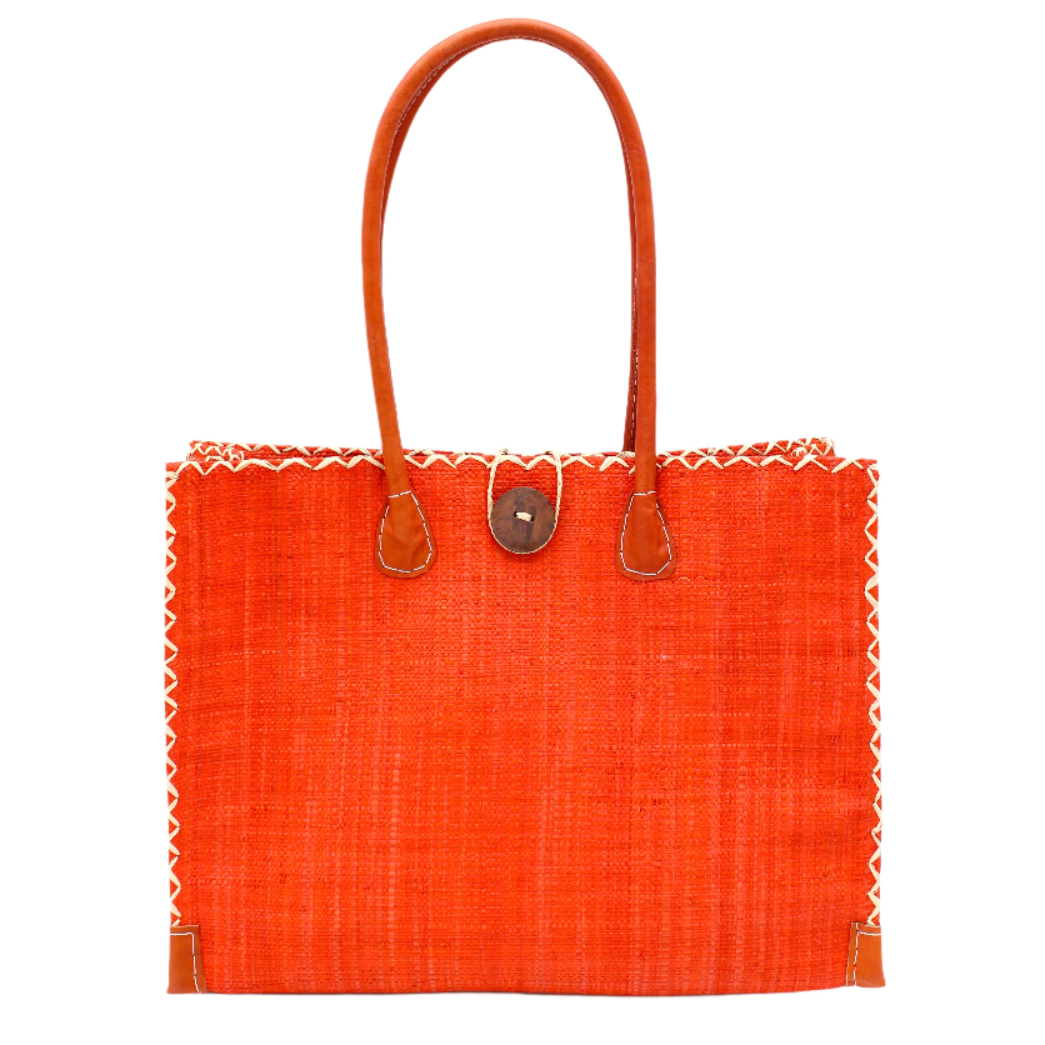 Zafran Straw Beach Bag with Plastic Liner handmade loomed raffia in a solid hue of Coral orange/red with contrasting natural straw color cross stitch edge binding, wood button closure, and leather handles & feet plus assorted print plastic lining - Shebobo