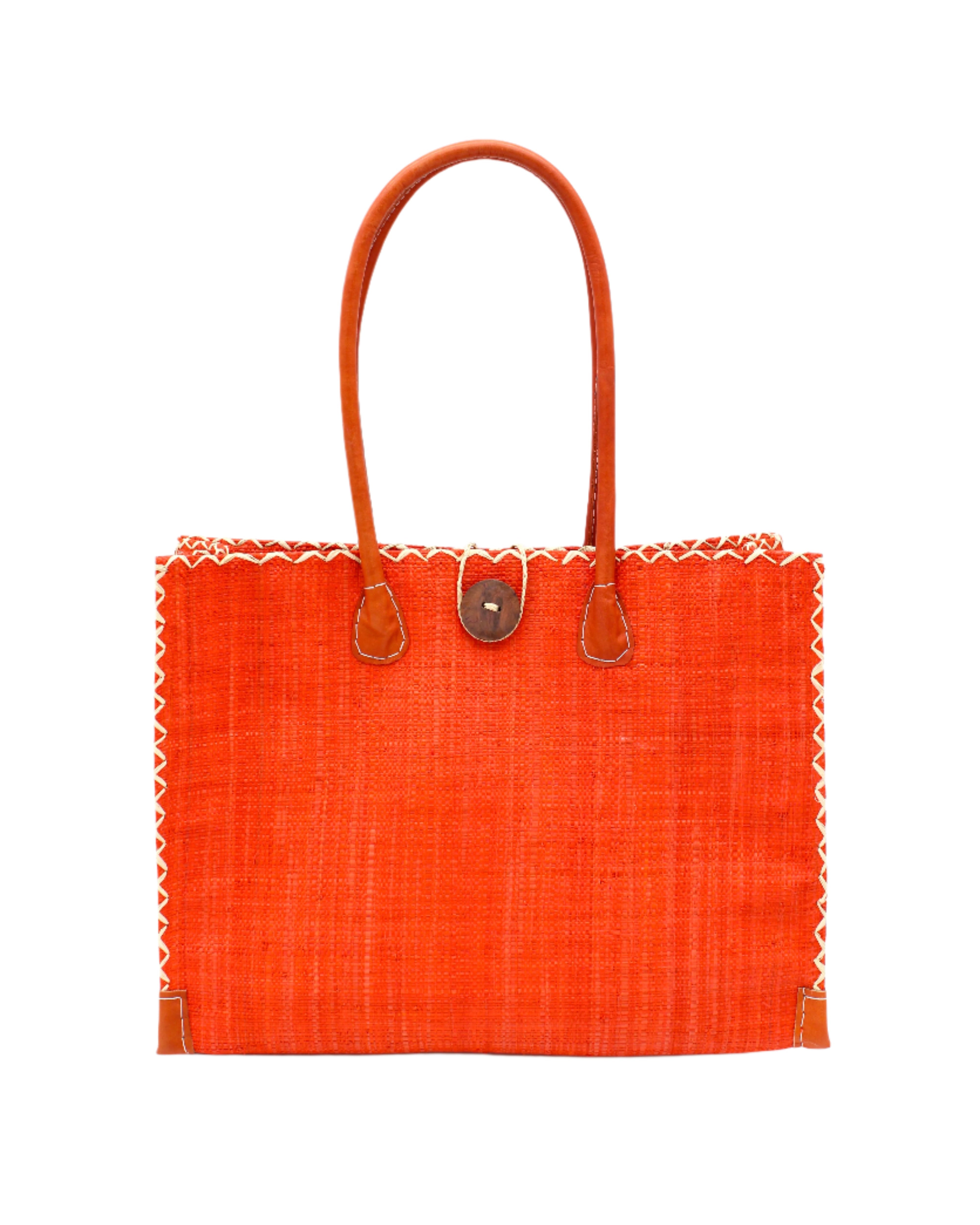 Zafran Straw Beach Bag with Plastic Liner handmade loomed raffia in a solid hue of Coral orange/red with contrasting natural straw color cross stitch edge binding, wood button closure, and leather handles & feet plus assorted print plastic lining - Shebobo