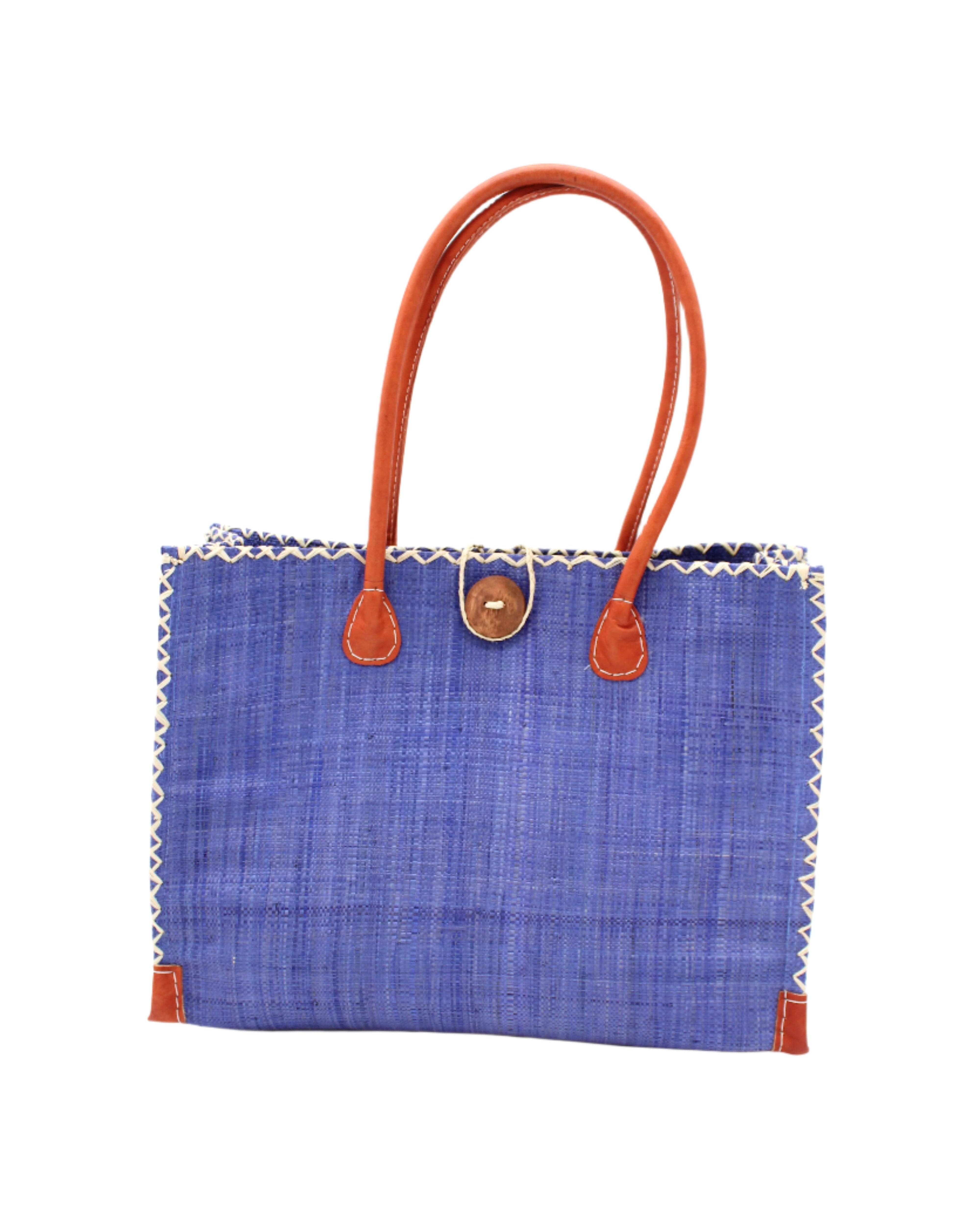 Zafran Straw Beach Bag with Plastic Liner handmade loomed raffia in a solid hue of Denim retro/light/blue with contrasting natural straw color cross stitch edge binding, wood button closure, and leather handles & feet plus assorted print plastic lining - Shebobo