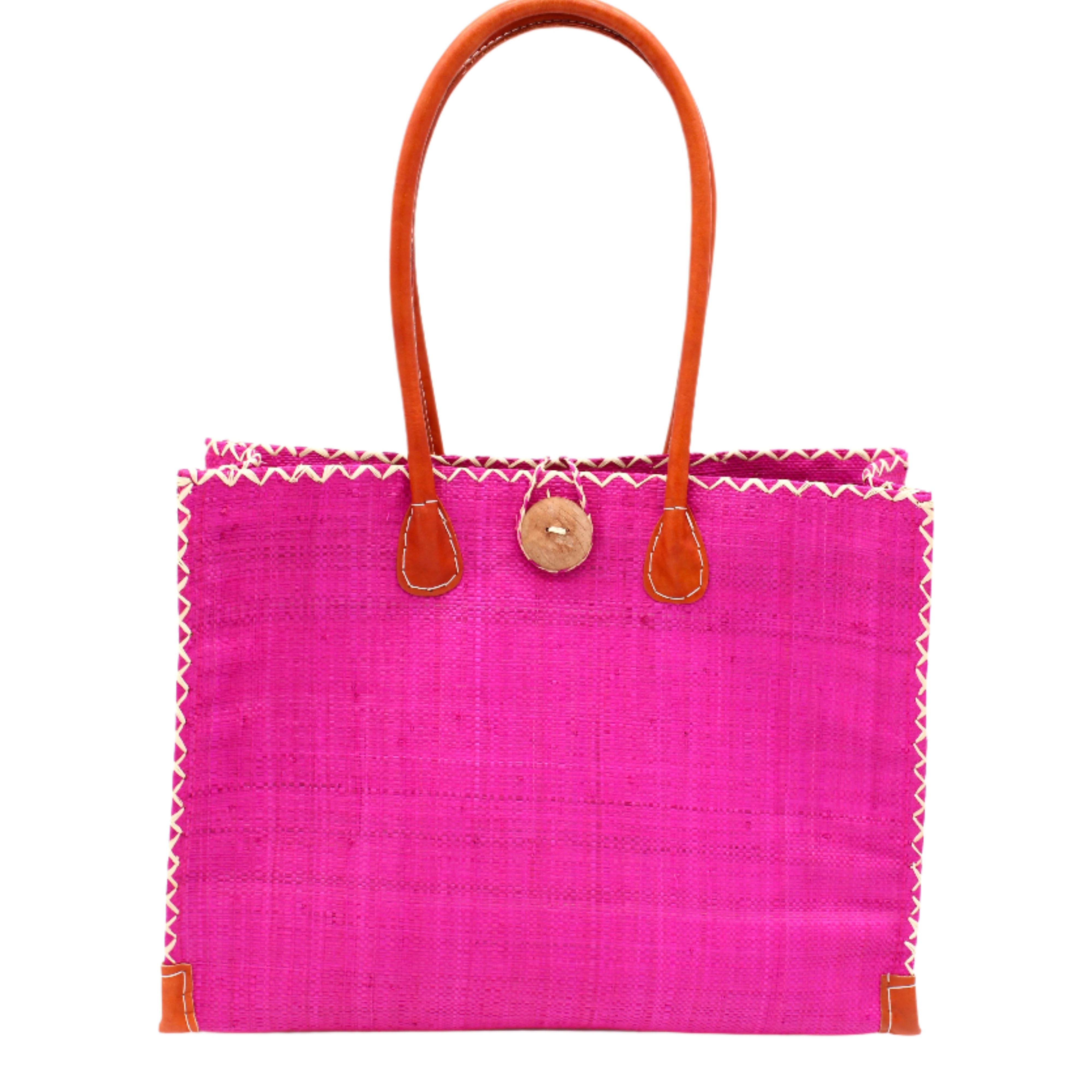 Zafran Straw Beach Bag with Plastic Liner handmade loomed raffia in a solid hue of Fuchsia hot/bright/barbie/pink with contrasting natural straw color cross stitch edge binding, wood button closure, and leather handles & feet plus assorted print plastic lining - Shebobo