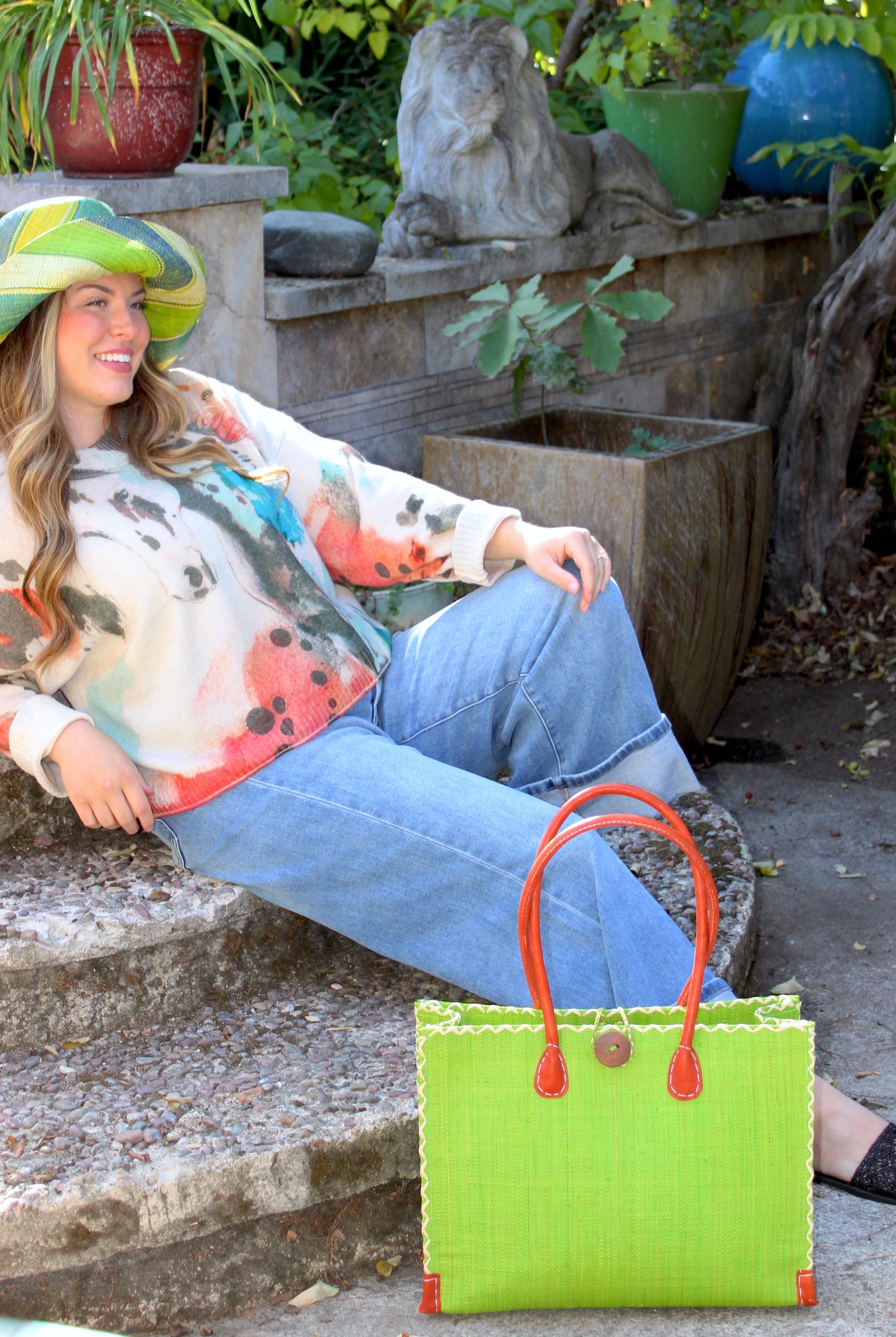 Model wearing Zafran Straw Beach Bag with Plastic Liner handmade loomed raffia in a solid hue of Midori lime/bright/neon/green with contrasting natural straw color cross stitch edge binding, wood button closure, and leather handles & feet plus assorted print plastic lining - Shebobo (with Monica 5" & 7" Wide Brim Multicolor Stripe Pattern Packable Straw Sun Hats)