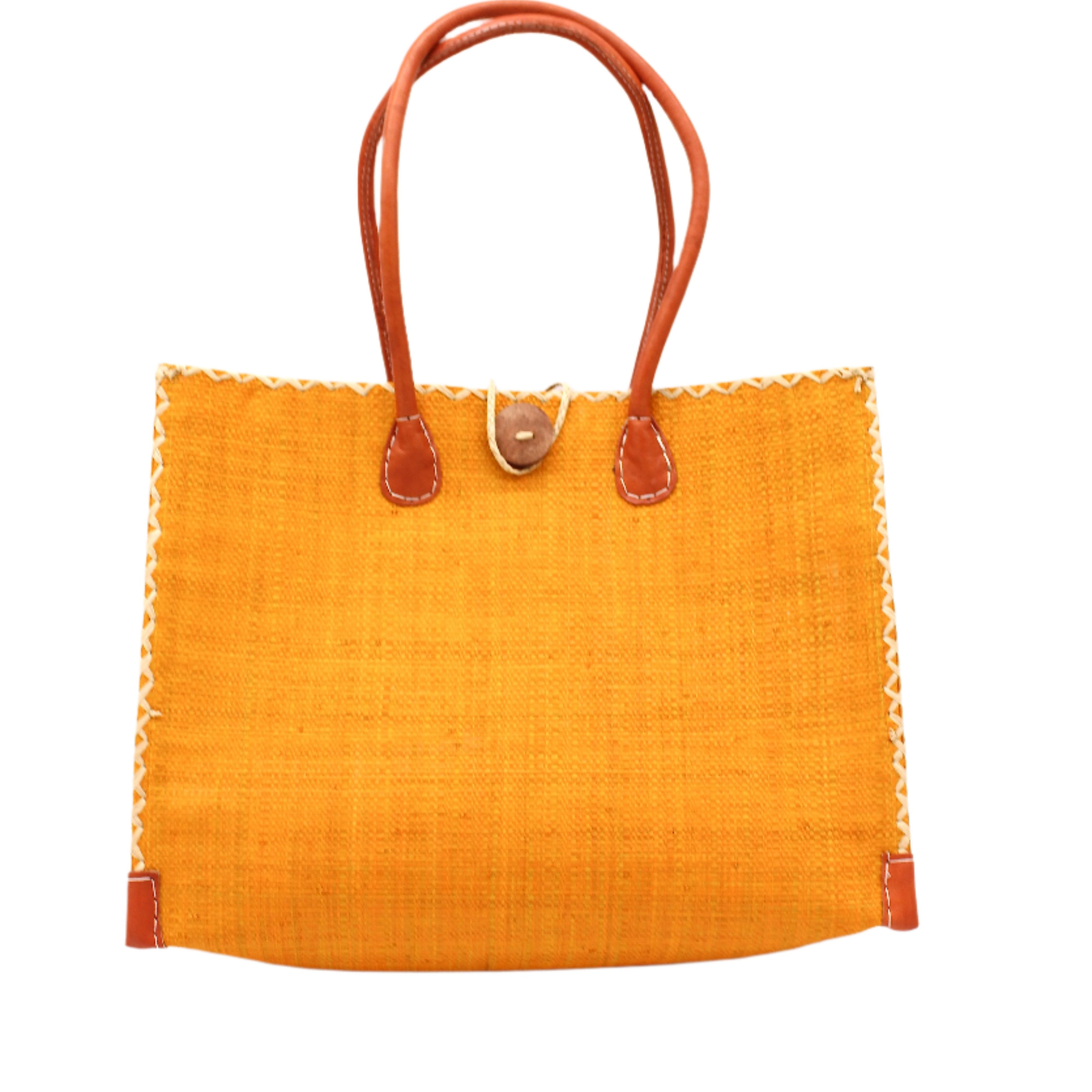 Zafran Straw Beach Bag with Plastic Liner handmade loomed raffia in a solid hue of saffron yellow/orange with contrasting natural straw color cross stitch edge binding, wood button closure, and leather handles & feet plus assorted print plastic lining - Shebobo