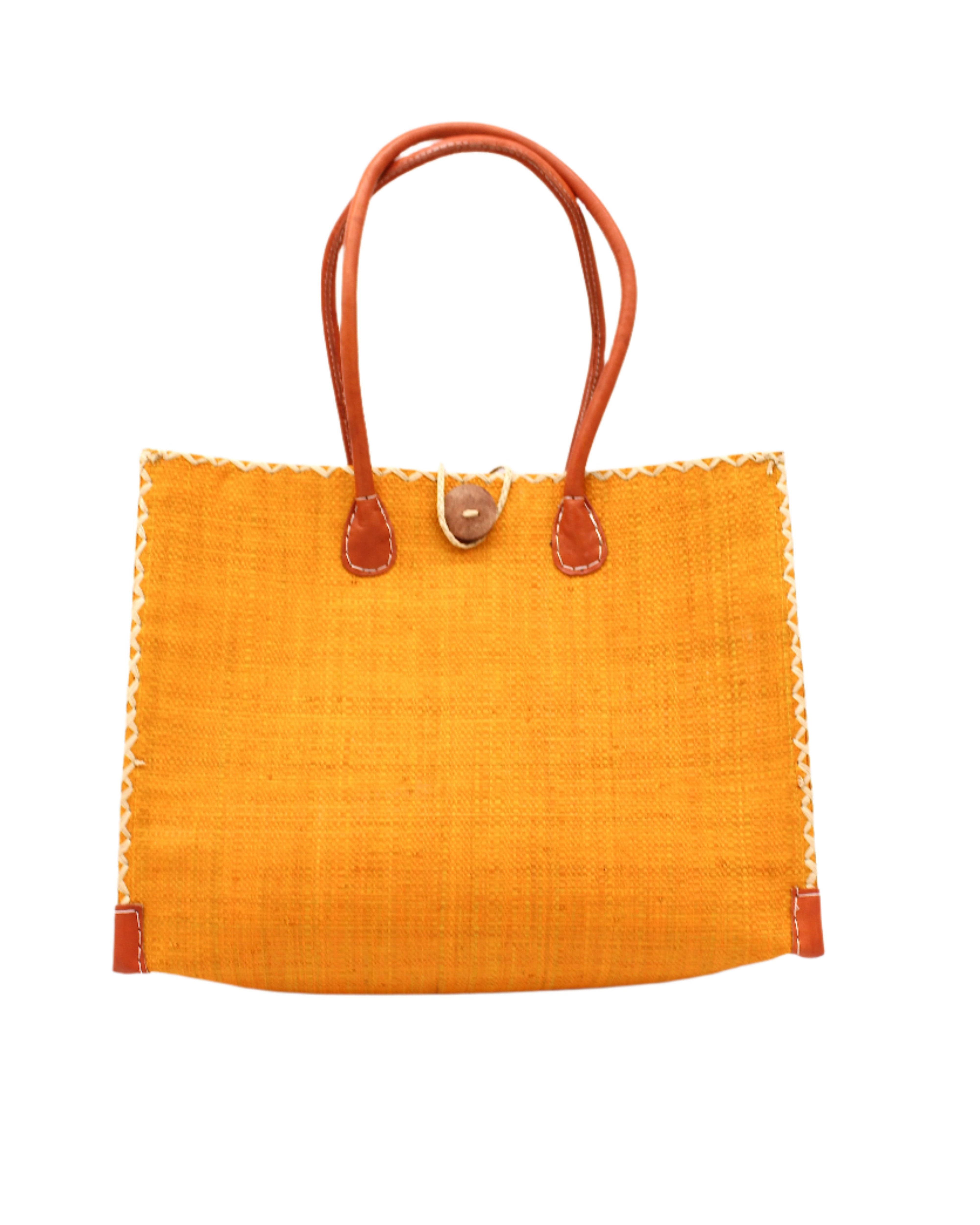 Zafran Straw Beach Bag with Plastic Liner handmade loomed raffia in a solid hue of saffron yellow/orange with contrasting natural straw color cross stitch edge binding, wood button closure, and leather handles & feet plus assorted print plastic lining - Shebobo
