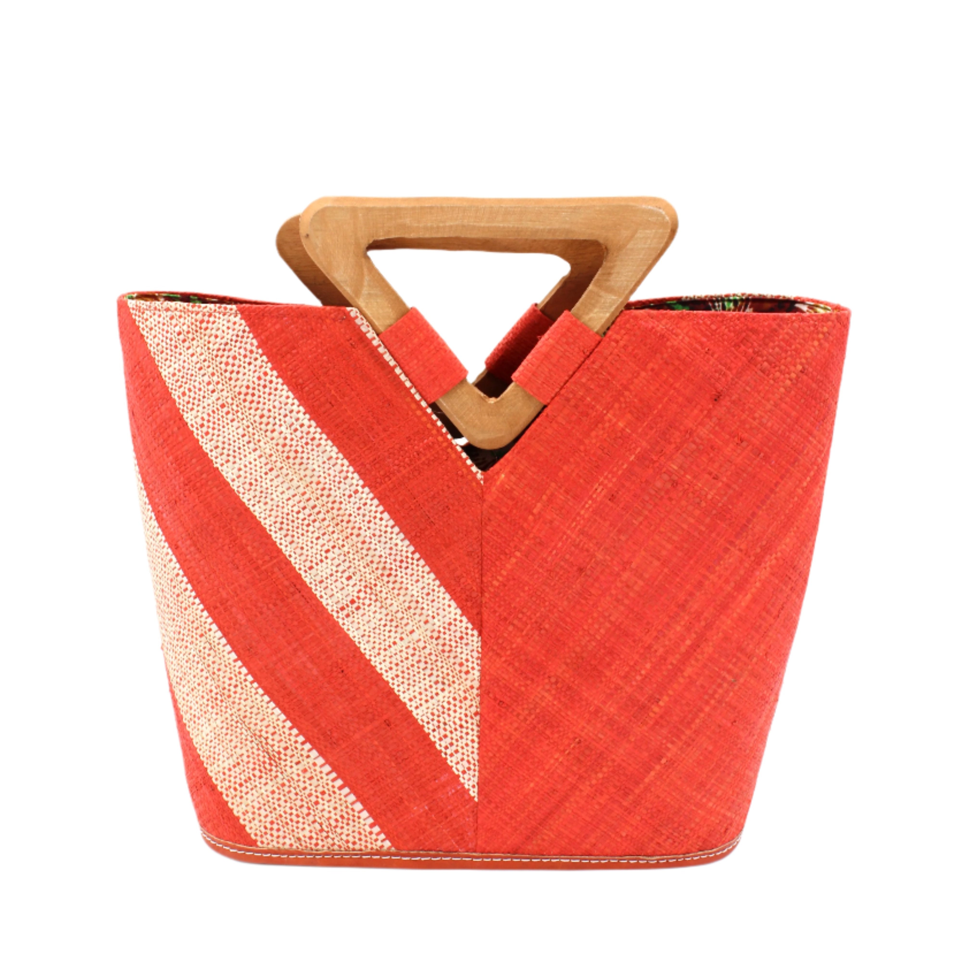 Zuki Two Tone Coral Straw Handbag With Wood Triangle Handle handmade loomed raffia palm fiber in a two tone pattern with the left half of the bag even width stripes of coral orange/red and natural straw color oriented as a diagonal stripe and the right half of the bag a solid hue of coral with carved wood handles - Shebobo
