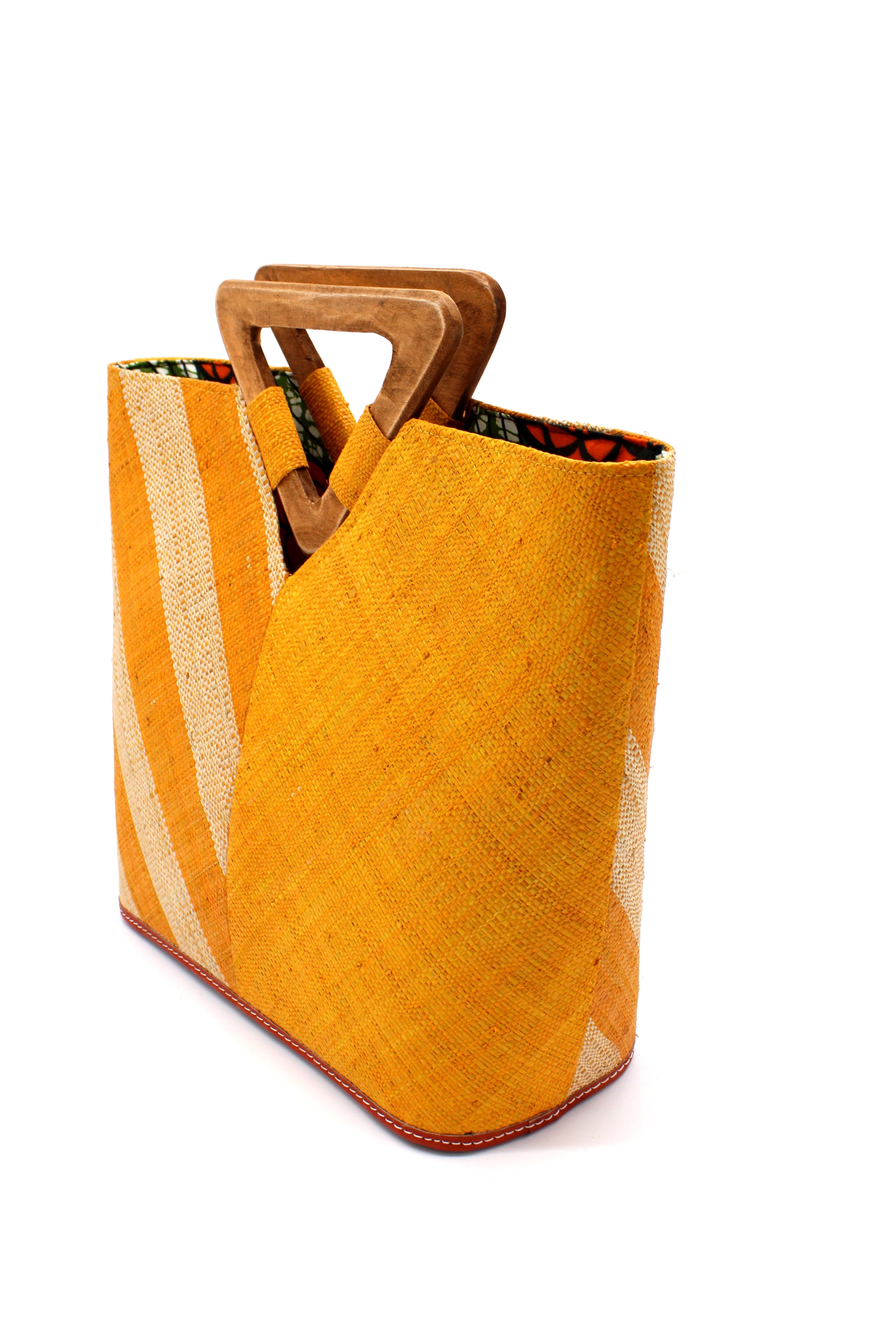 Side View Zuki Two Tone Saffron Straw Handbag With Wood Triangle Handle handmade loomed raffia palm fiber in a two tone pattern with the left half of the bag even width stripes of saffron yellow/orange and natural straw color oriented as a diagonal stripe and the right half of the bag a solid hue of saffron with carved wood handles - Shebobo