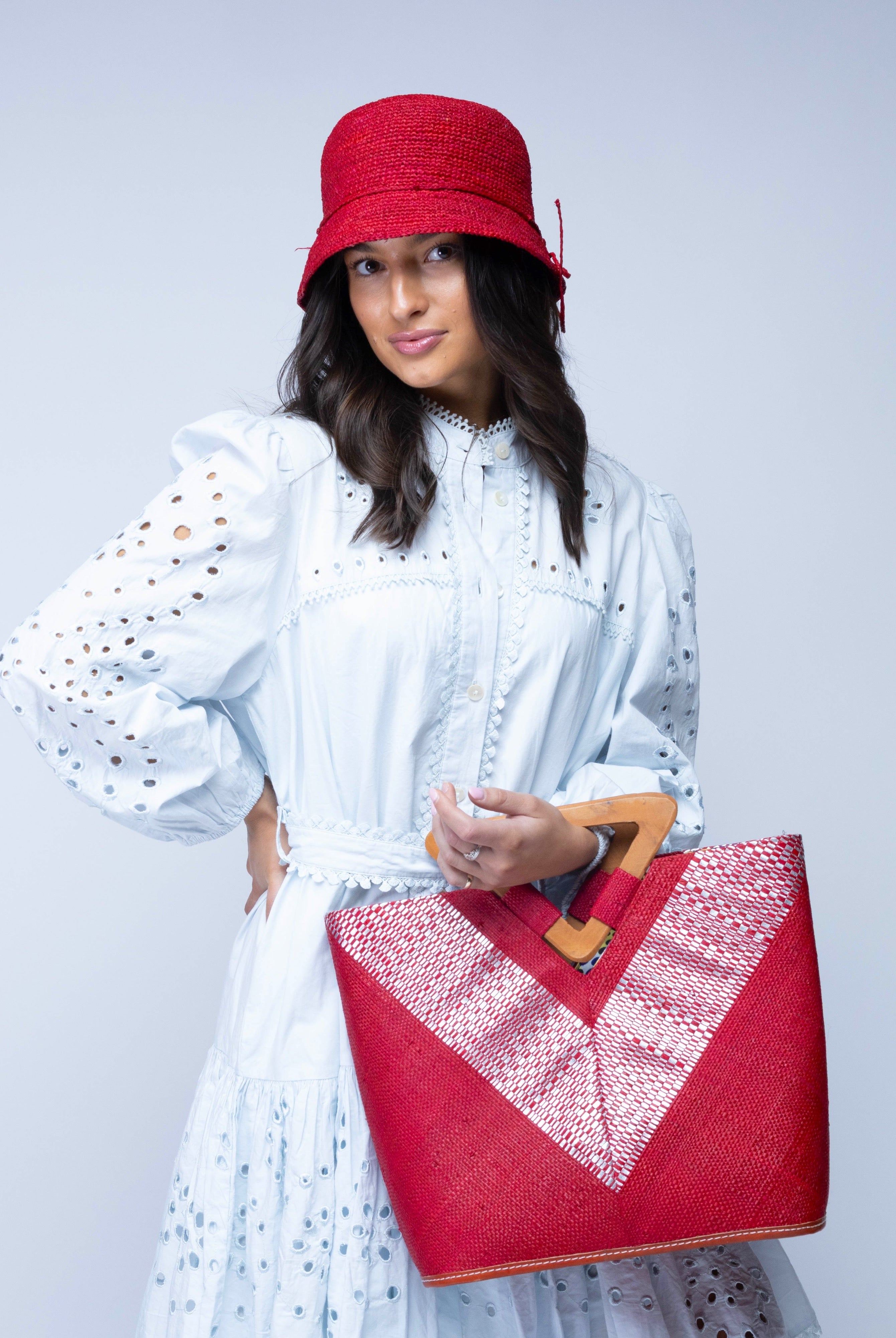 Model wearing Zuki Wynwood Red Straw Handbag with Metallic Detailing & Wood Triangle Handle handmade loomed raffia palm fiber in a solid hue of red with incorporated vegan leather silver metallic strands in a V pattern across the front and back of the bag with assorted print African wax cloth liners and carved wooden triangle handle purse - Shebobo