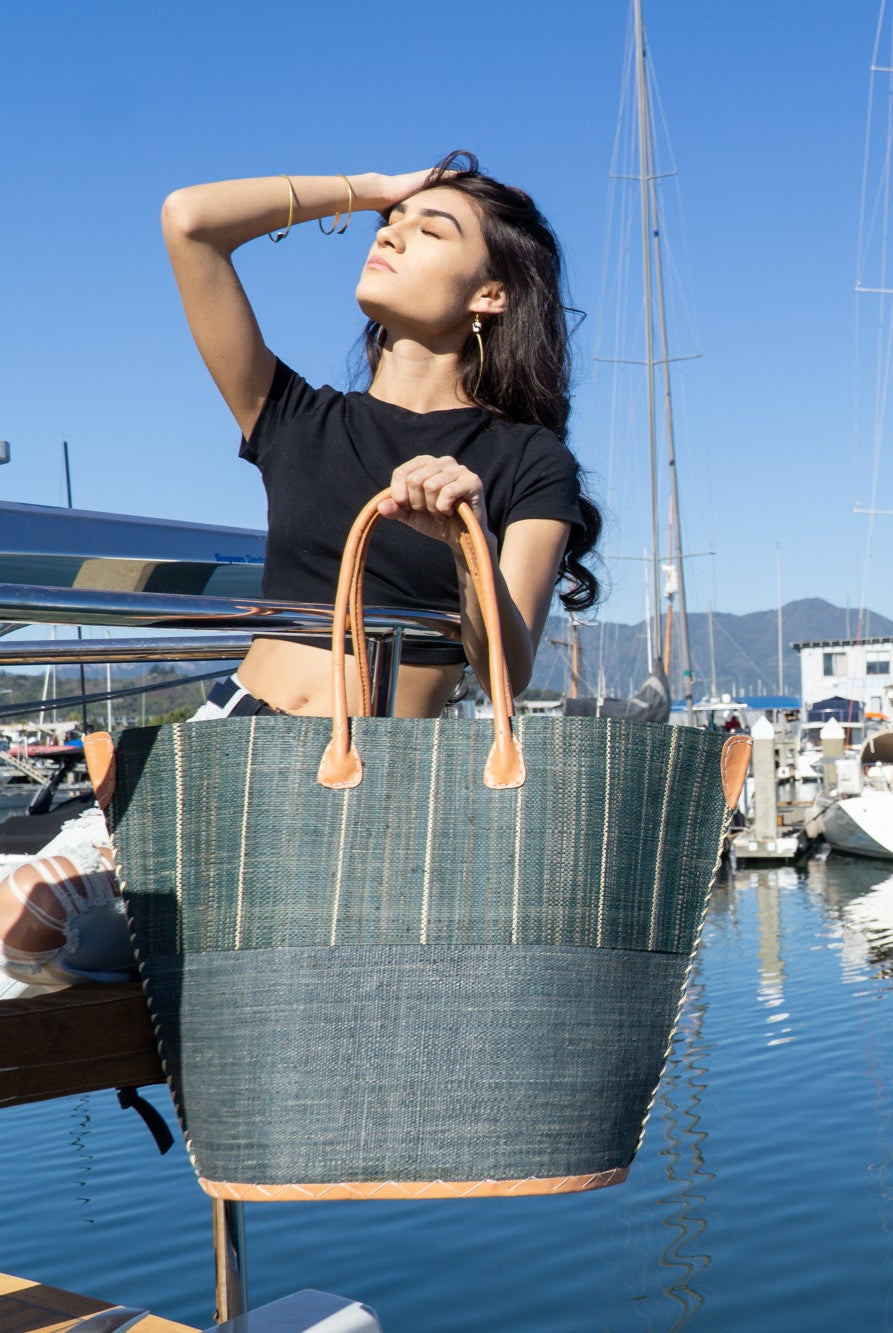 model wearing Santa Cruz Two Tone Large Straw Tote Bag handmade beach bag loomed raffia solid grey bottom with grey and natural vertical pinstripe pattern top plus leather handles xl handbag - Shebobo