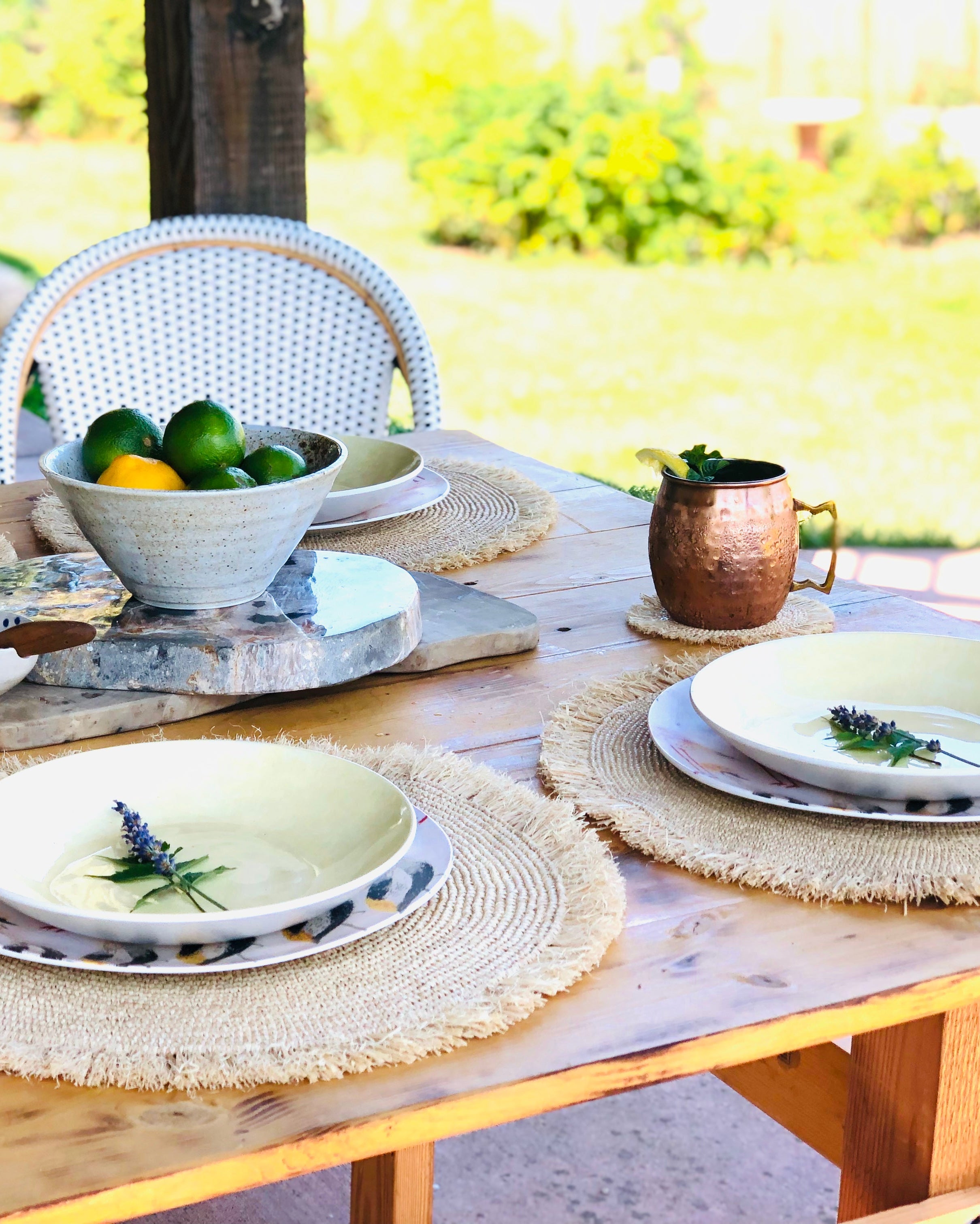 Imani Crochet raffia coasters set of 4 shown with outdoor table setting with matching placemats home decor handmade natural raffia palm fiber crochet in a solid hue of natural straw color in a subtle spiral texture disc with brushed fringe edge - Shebobo