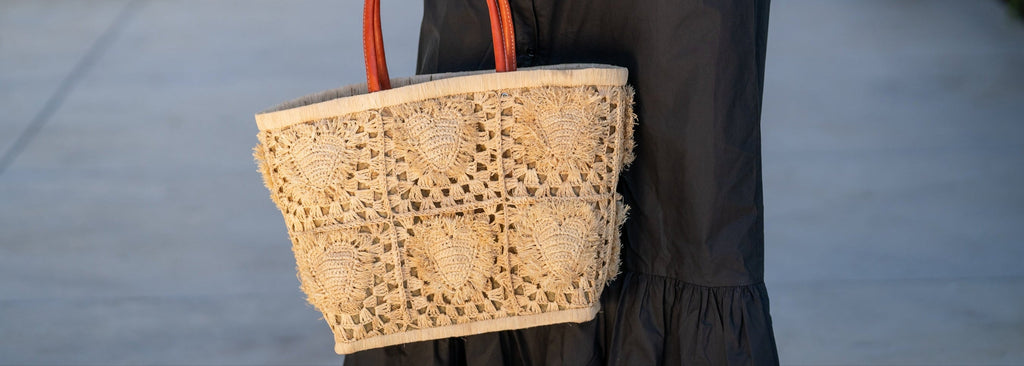 Model wearing Hearts Crochet Straw Basket Bag with Fringed Heart Pattern handmade woven raffia in a solid hue of natural straw color with granny square pattern and raised/stuffed heart pattern & leather handles purse beach bag shoulder bag - Shebobo 