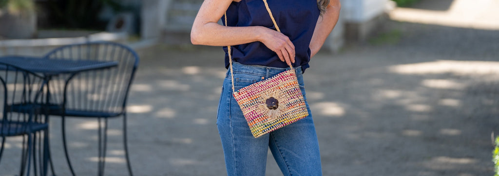 Model wearing Barbados Crochet Straw Crossbody Bag with Flower Detail handmade crochet raffia palm fiber in a loop technique creating horizontal concentric multicolor wrapped bands with assorted combined colors purse - Shebobo
