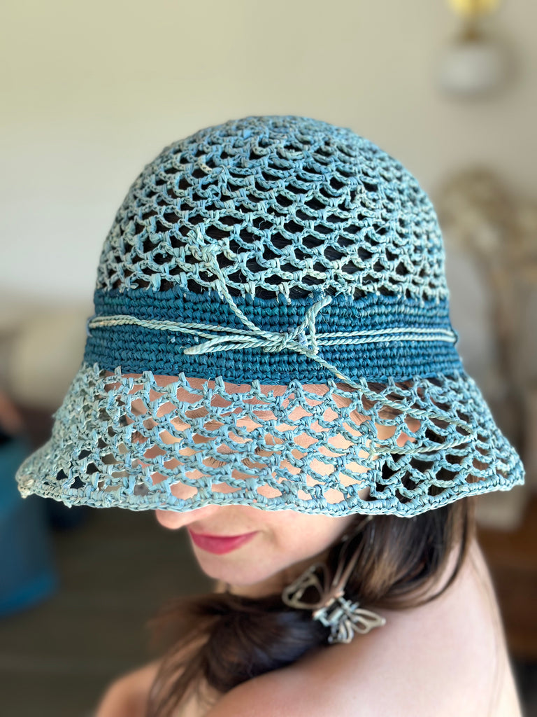 Model wearing 2.5" Brim Maria Blue Crochet Bucket Straw Hat handmade raffia palm fiber crochet in an open loop wave/shell pattern of baby light blue with a close weave crochet hat band in contrasting dark turquoise blue with adjustable hat band straw sun hat - Shebobo