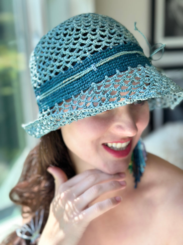 Model wearing 2.5" Brim Maria Blue Crochet Bucket Straw Hat handmade raffia palm fiber crochet in an open loop wave/shell pattern of baby light blue with a close weave crochet hat band in contrasting dark turquoise blue with adjustable hat band straw sun hat - Shebobo