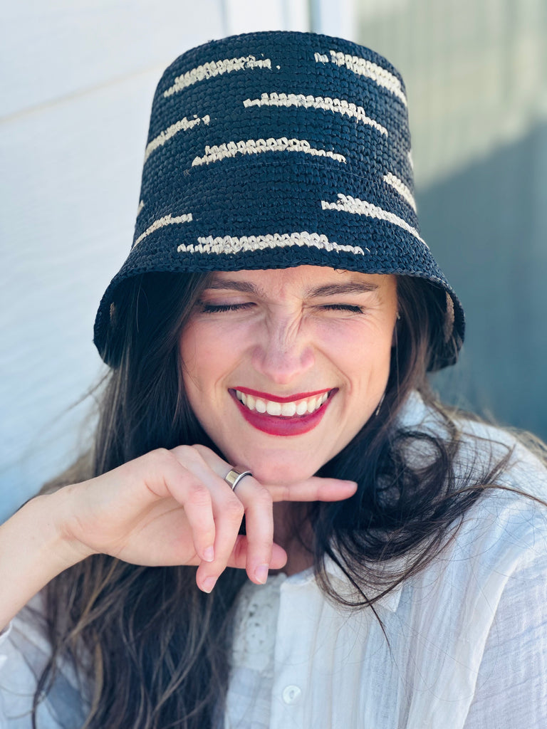 Model wearing 2.5" Brim Taylor Black Crochet Bucket Straw Hat with Zebra Stripes handmade raffia palm fiber in a two tone color combination of horizontal short stripes that create a dash pattern around the hat in black with natural straw color - Shebobo